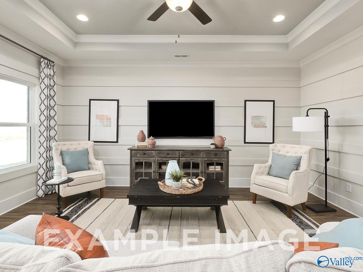 Cozy living room with beige armchairs, wooden console table, mounted TV, ceiling fan in Davidson Homes The Everett B, Toney, Alabama