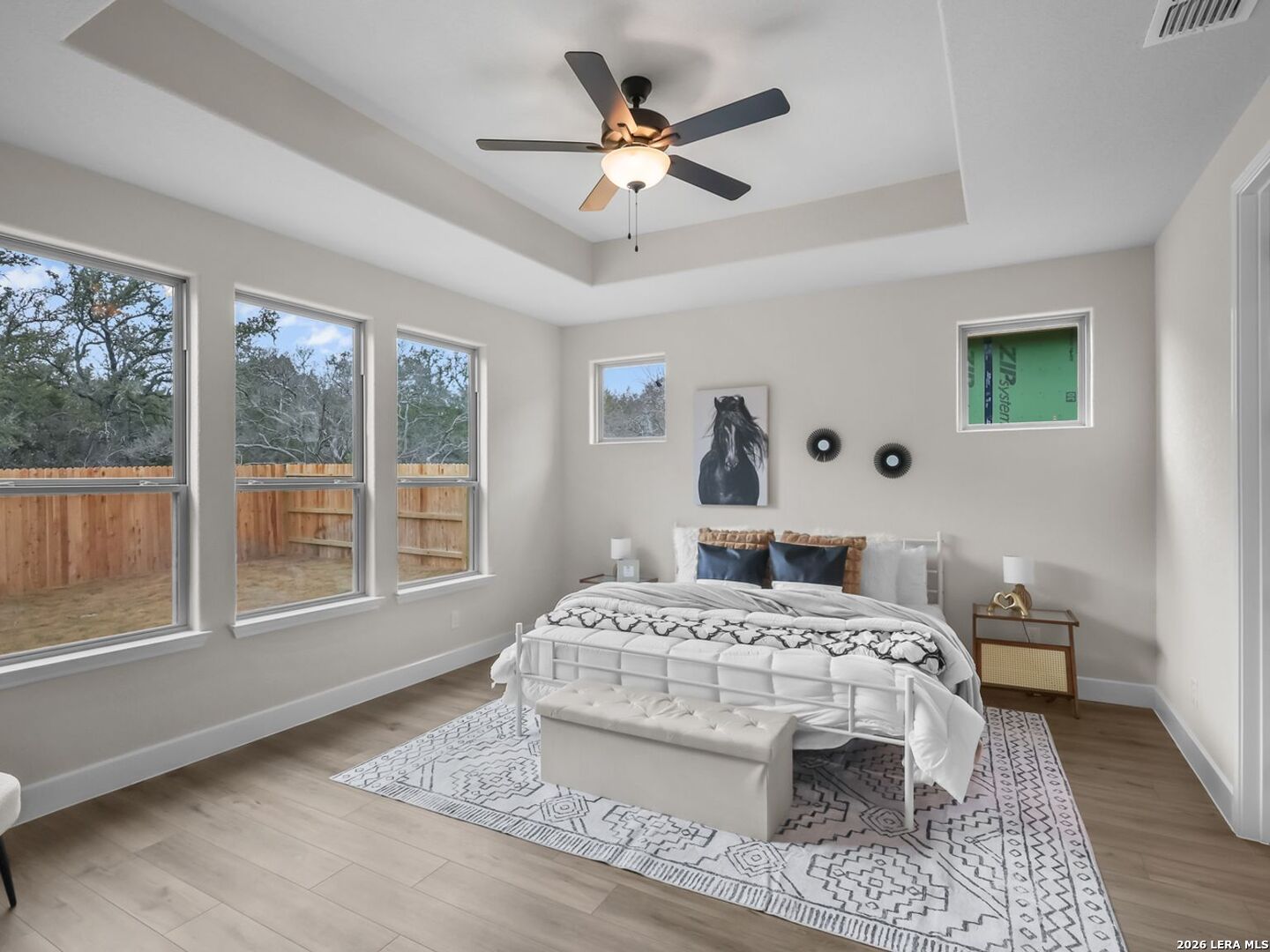 Primary bedroom with tray ceiling and large windows in The Belmont H floor plan at Potranco Oaks, Castroville, Texas.