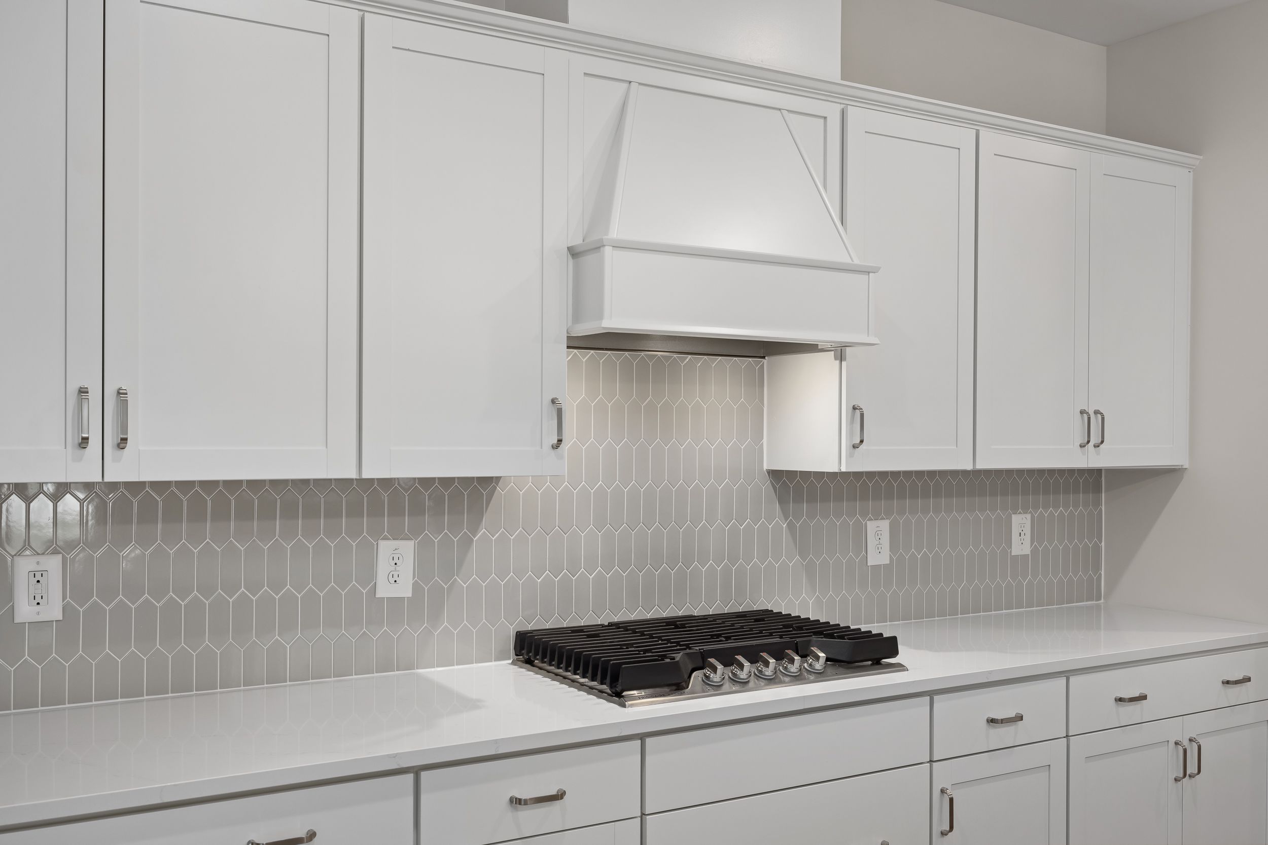 Modern Beech A kitchen featuring white shaker cabinets, hexagonal gray subway tile backsplash, and gas range
