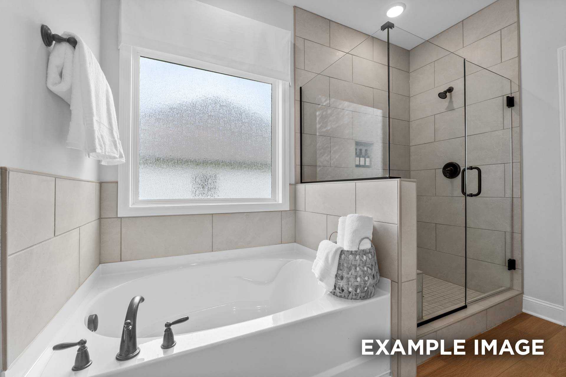 Spacious master bathroom in The Laurel N featuring soaking tub, glass shower enclosure, tiled walls, and frosted window