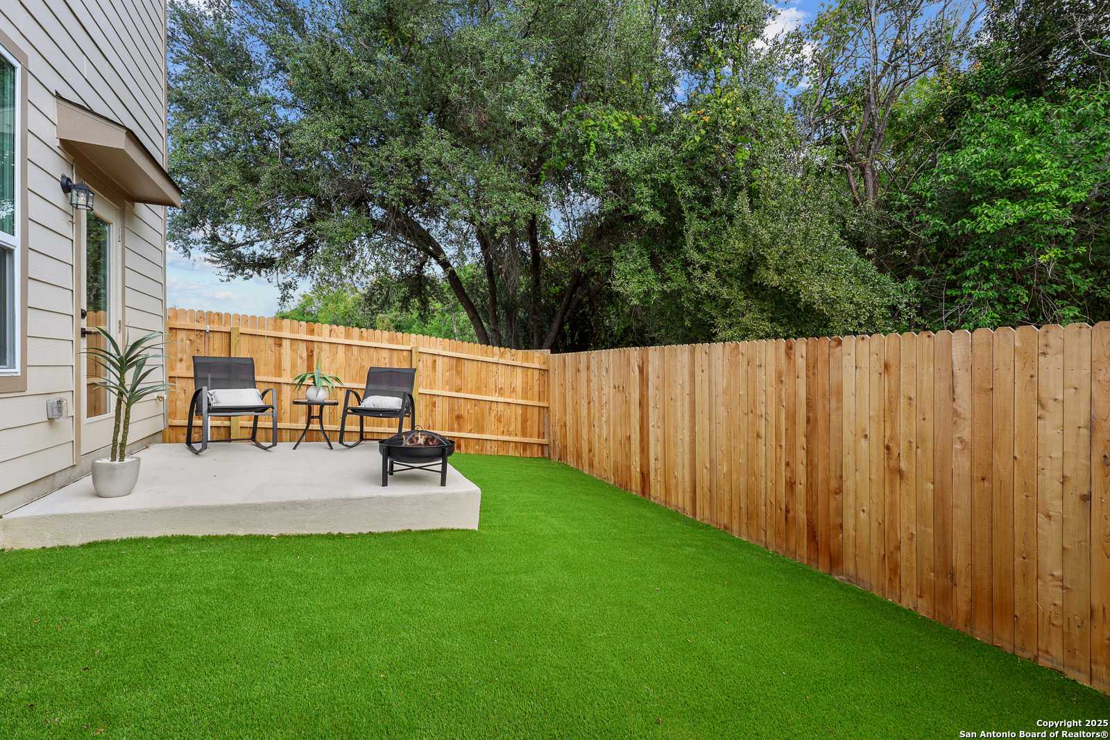 Cozy backyard patio with Adirondack chairs, fire pit, artificial turf, and wooden fence in Davidson Homes The Charlotte B, Cedar Heights, San Antonio