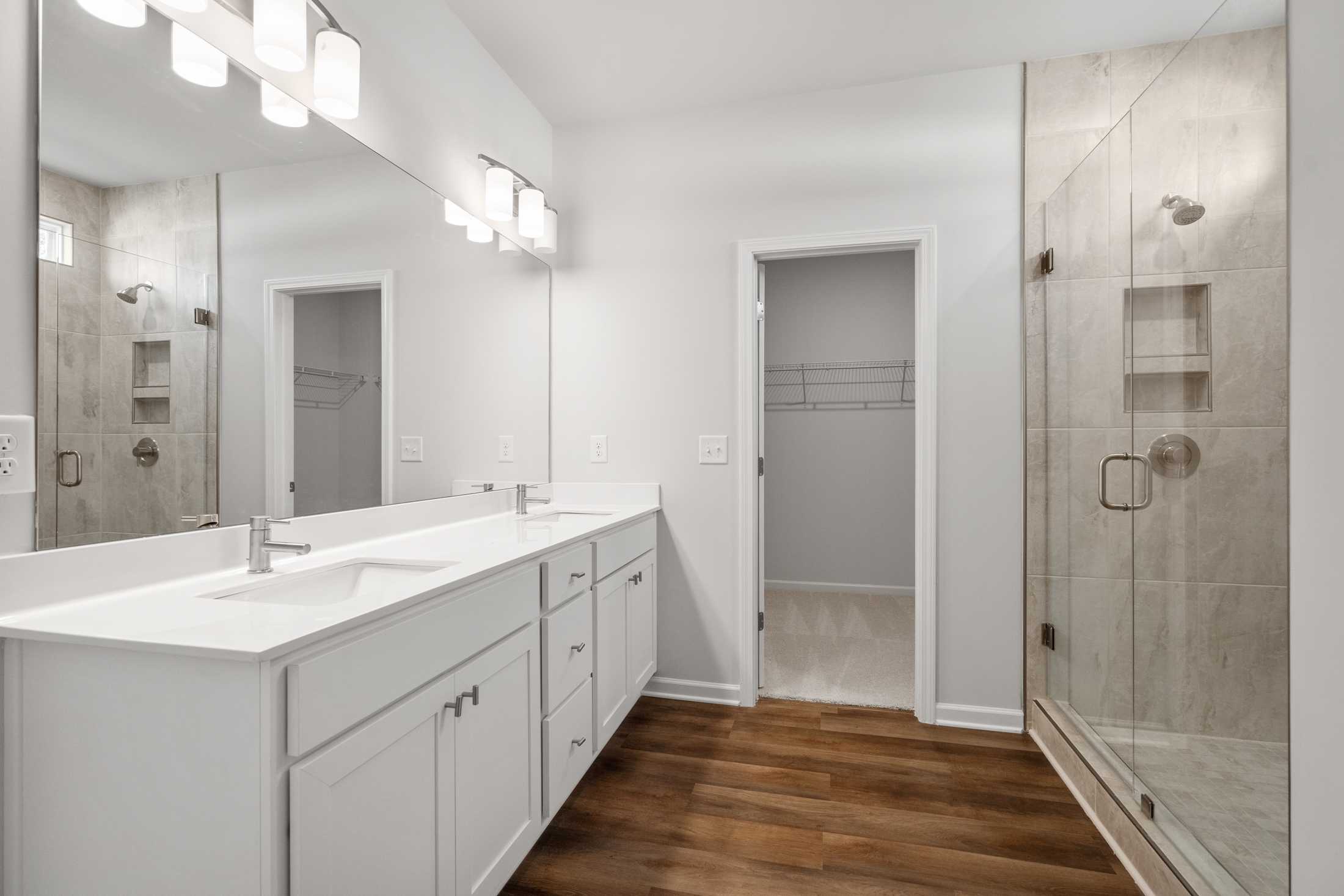 Spacious primary bathroom at Everleigh in Locust Grove GA with double white vanity, frameless glass shower, and hardwood floors
