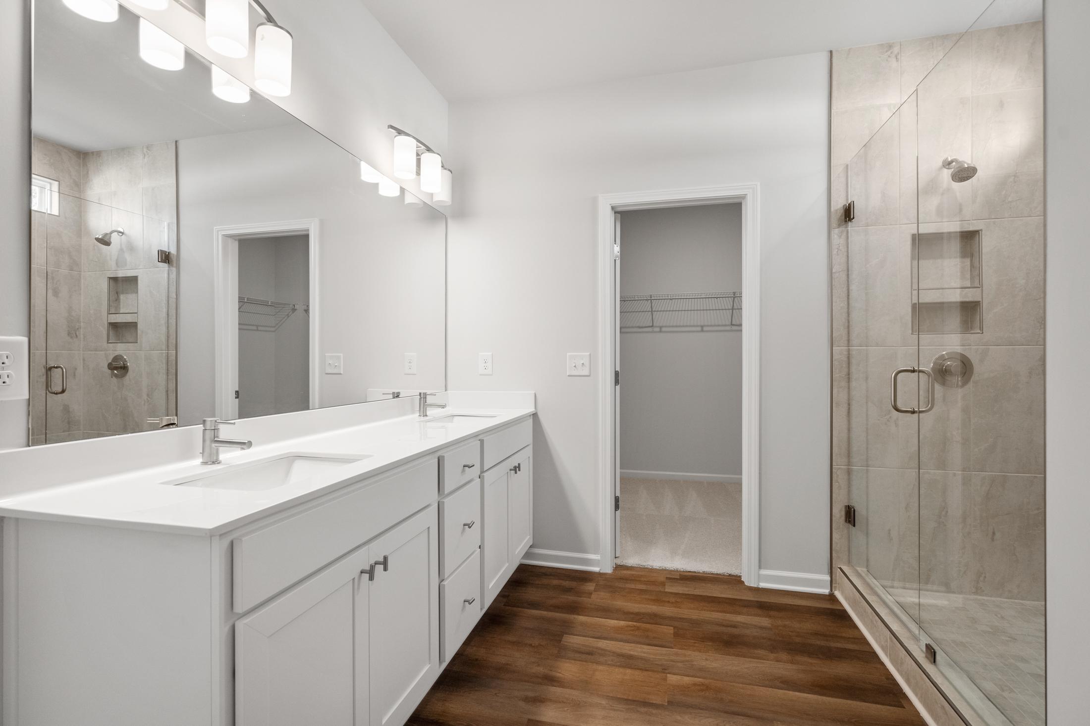 Spacious primary bathroom at Everleigh in Locust Grove GA with double white vanity, frameless glass shower, and hardwood floors