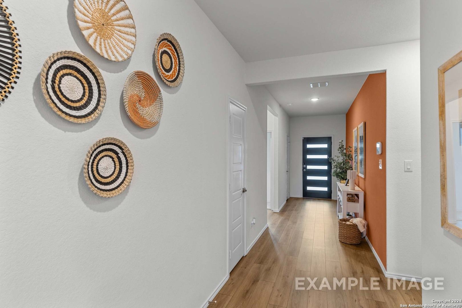 Entry hallway featuring woven baskets on walls, orange accent, hardwood floors in Davidson Homes The Daphne K, San Antonio