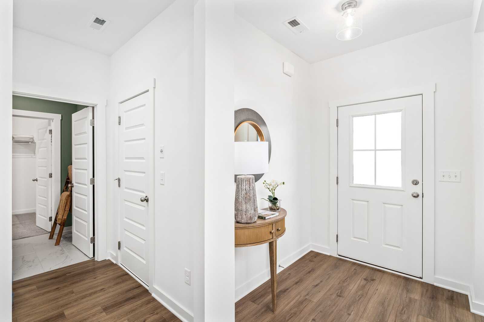 Bright entryway and hallway in Calista Farms White House TN home with hardwood floors, round mirror, console table, and white glass-paneled door