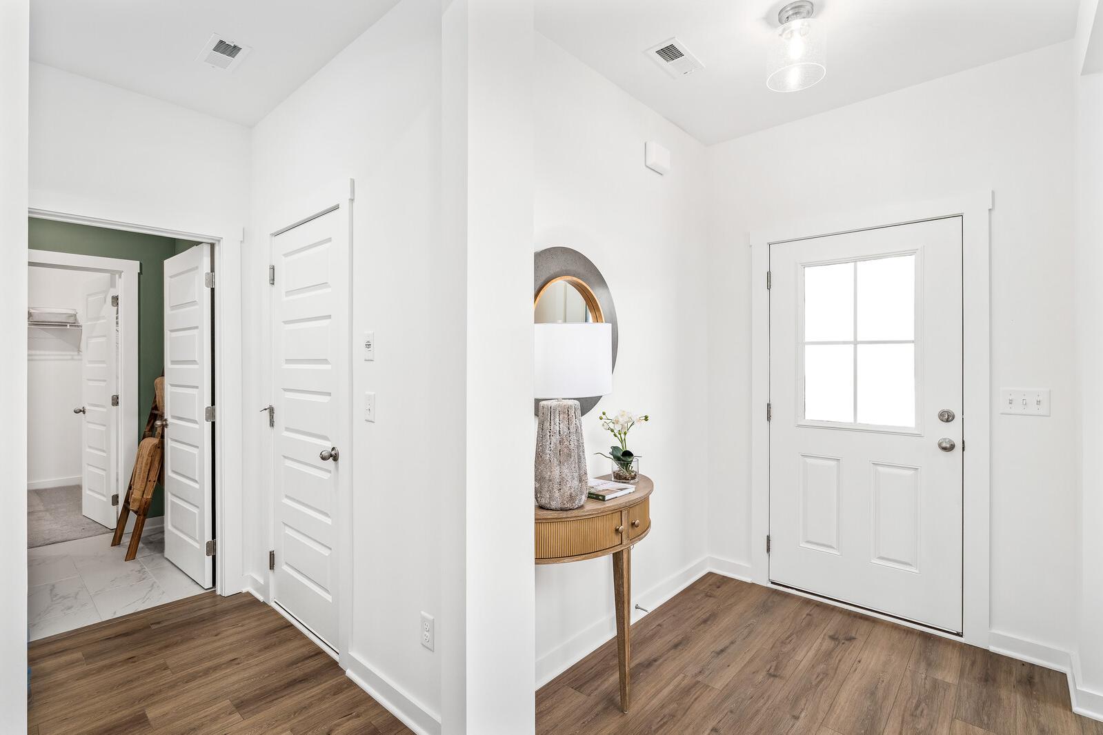 Bright entryway and hallway in Calista Farms White House TN home with hardwood floors, round mirror, console table, and white glass-paneled door