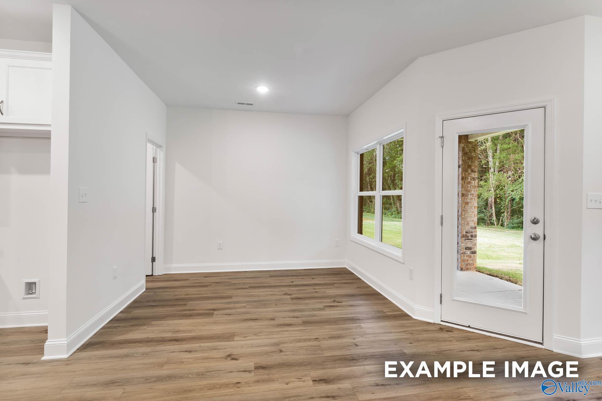 Bright open living area with white walls, hardwood floors, large windows, and glass door to wooded backyard in The Daphne V home, Athens, Alabama