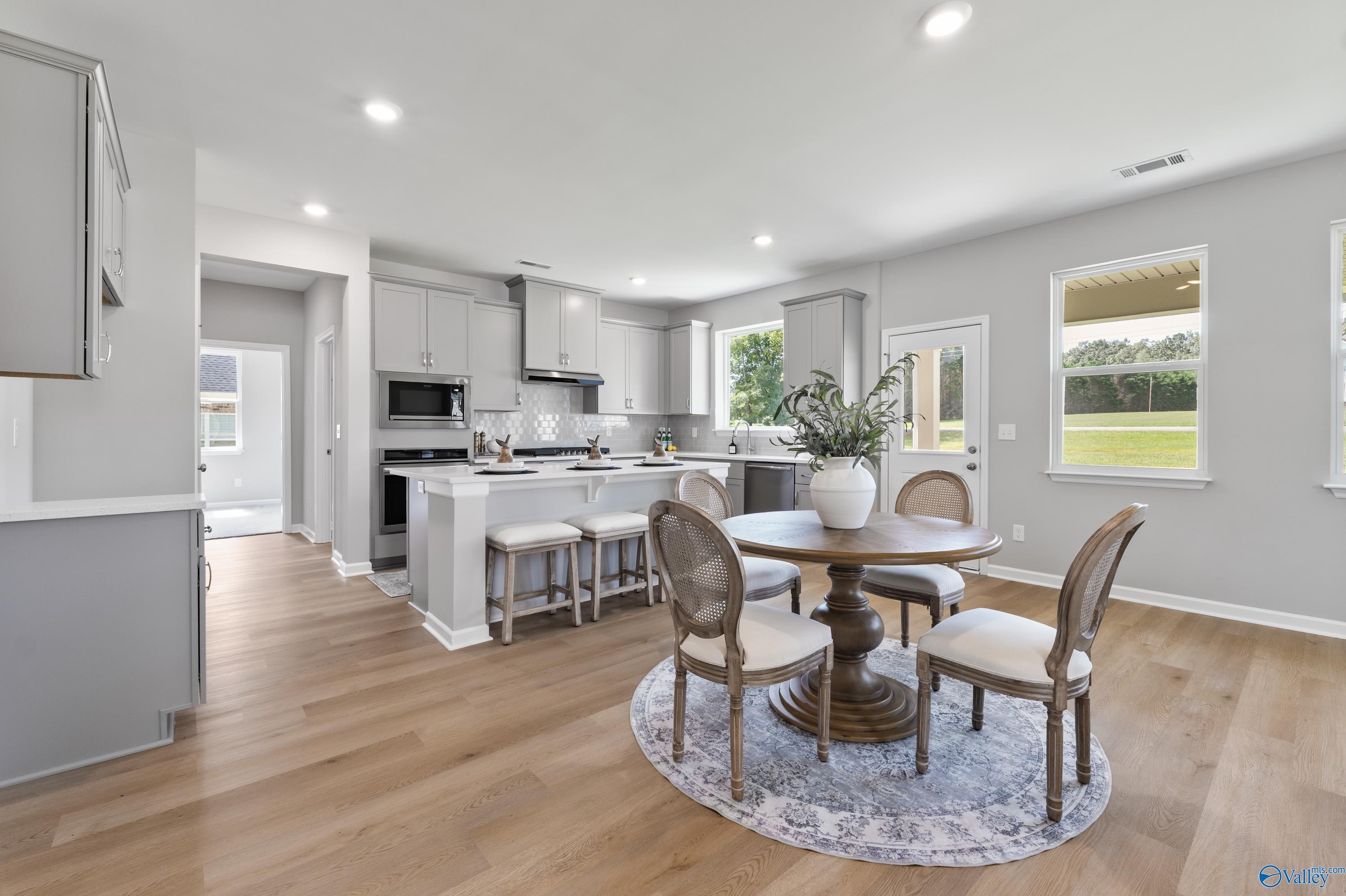 Open-concept kitchen with gray cabinets, white counters, stainless appliances, and round dining table in The Charm 4-bedroom home, Huntsville, Alabama