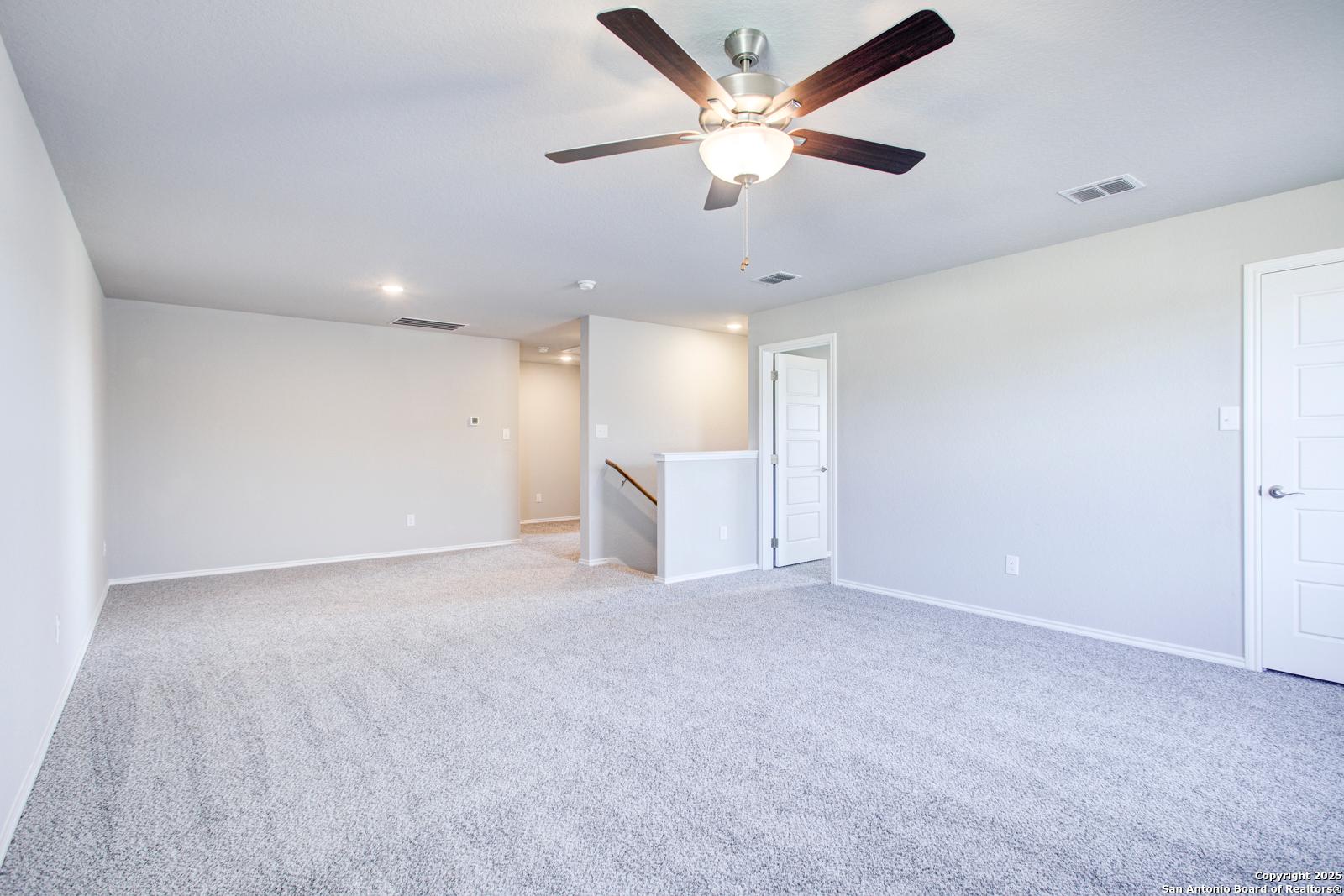 Spacious two-story foyer with gray carpet, ceiling fan, staircase, and doors in Davidson Homes The Douglas G, San Antonio