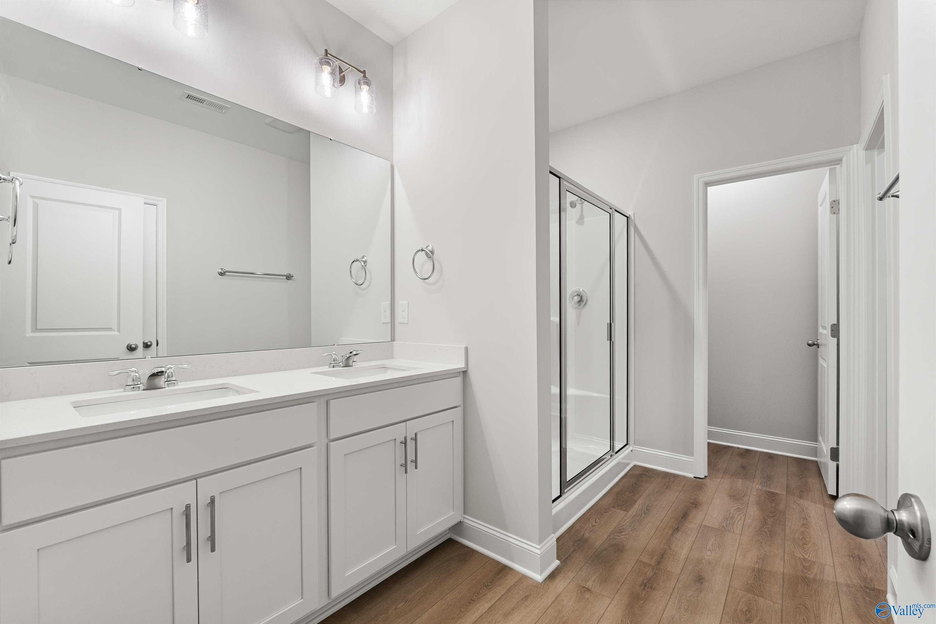 Modern master bathroom featuring double white vanity, large mirror, glass shower, and wood floors in Davidson Homes The Daphne, Huntsville, AL