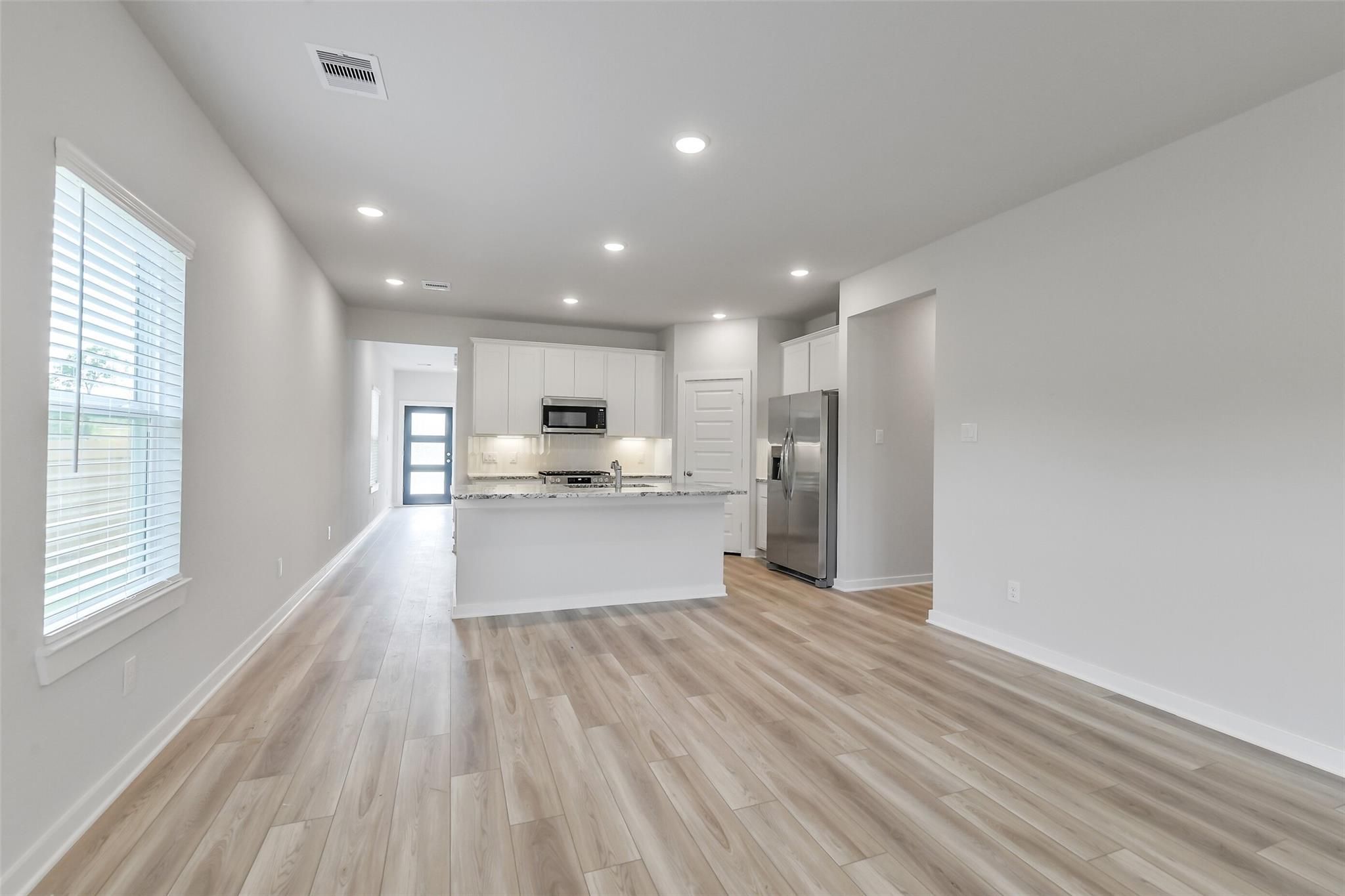 Modern open-concept kitchen with white cabinets, stainless steel fridge, granite island, and wood flooring in The San Marcos E, Conroe, Texas
