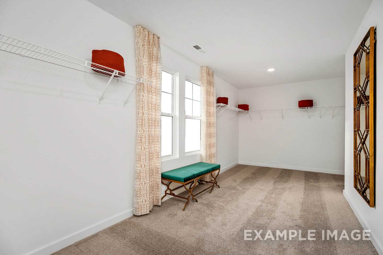 Spacious walk-in closet in The Gordon B master suite with built-in shelving, hanging rods, green bench, and large mirror