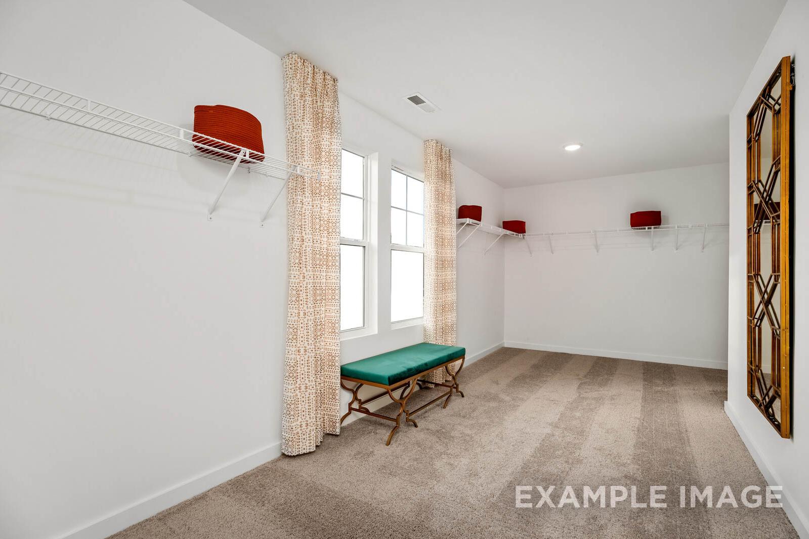 Spacious walk-in closet in The Gordon C master suite with built-in rods, green bench, and ornate mirror