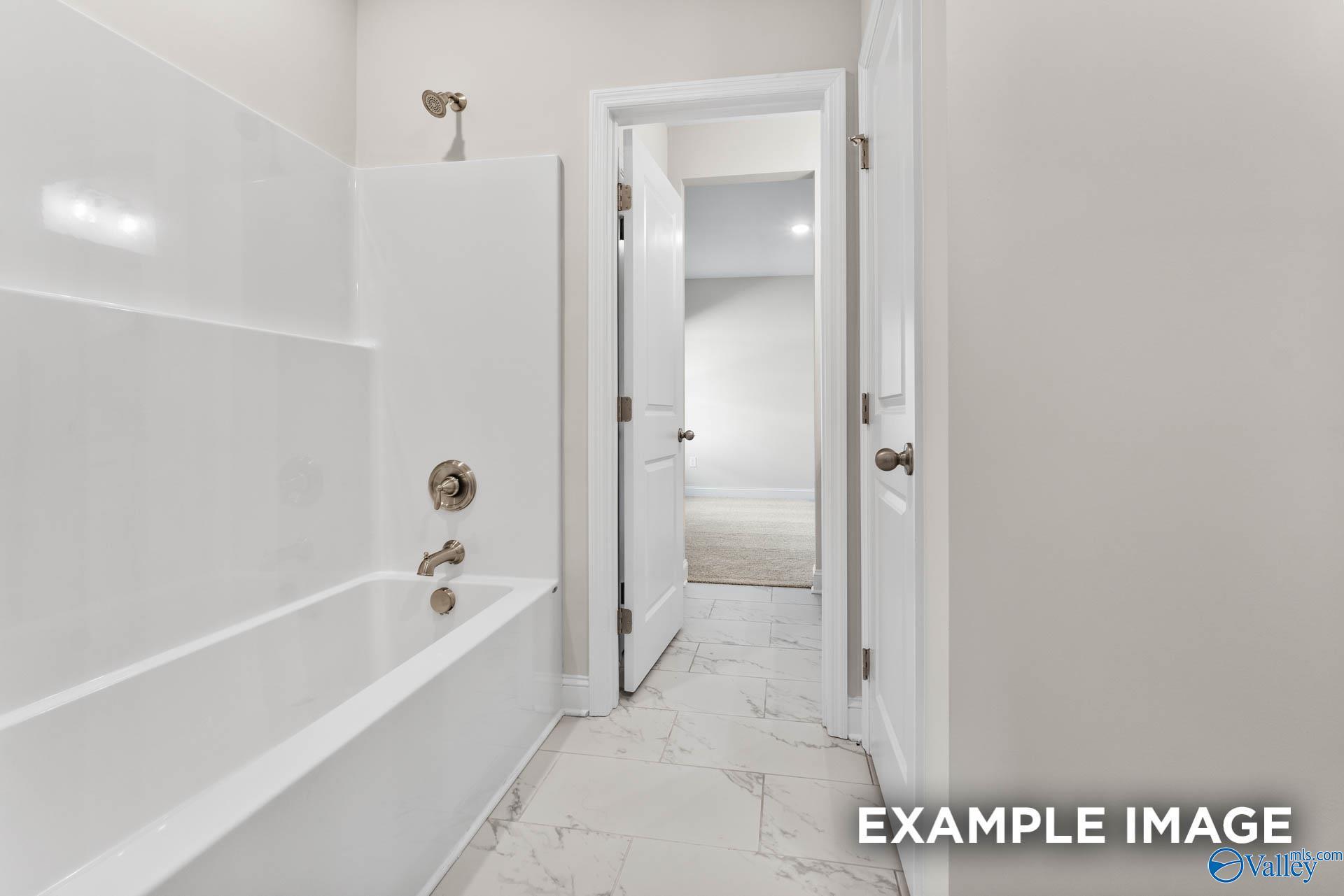 Bright bathroom with white tub-shower combo, porcelain tile floor, and hallway access in Davidson Homes The Finleigh, Huntsville, Alabama