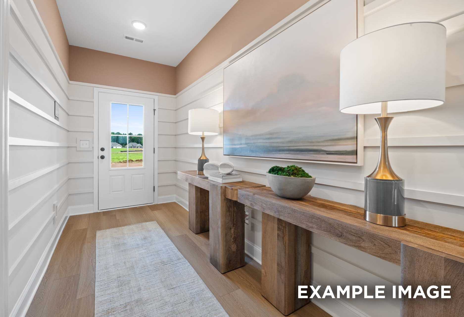 Elegant foyer in The Laurel M home: shiplap walls, abstract seascape art, wooden consoles with lamps, potted plant, baseball field view through door