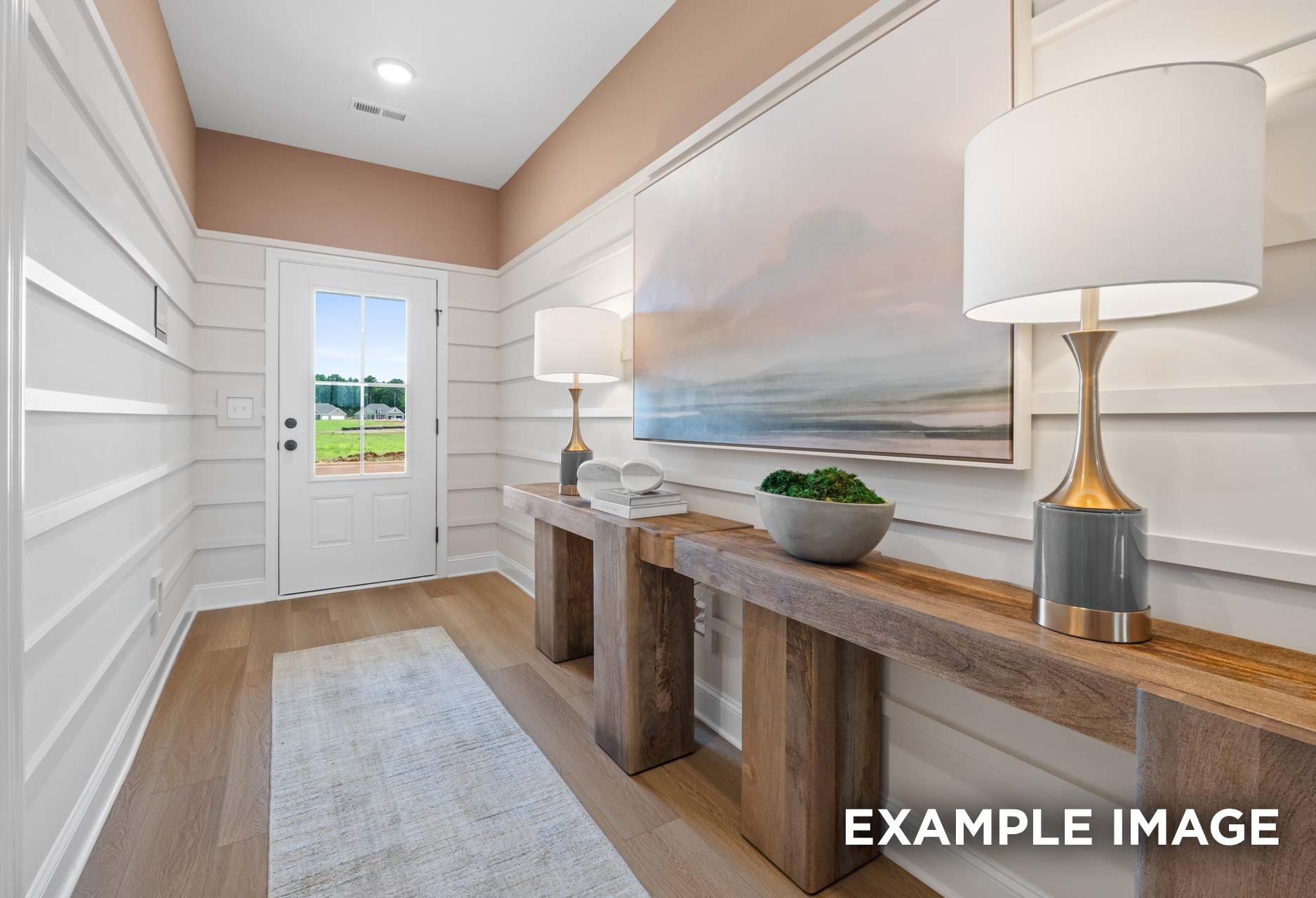 Elegant foyer in The Laurel M home: shiplap walls, abstract seascape art, wooden consoles with lamps, potted plant, baseball field view through door