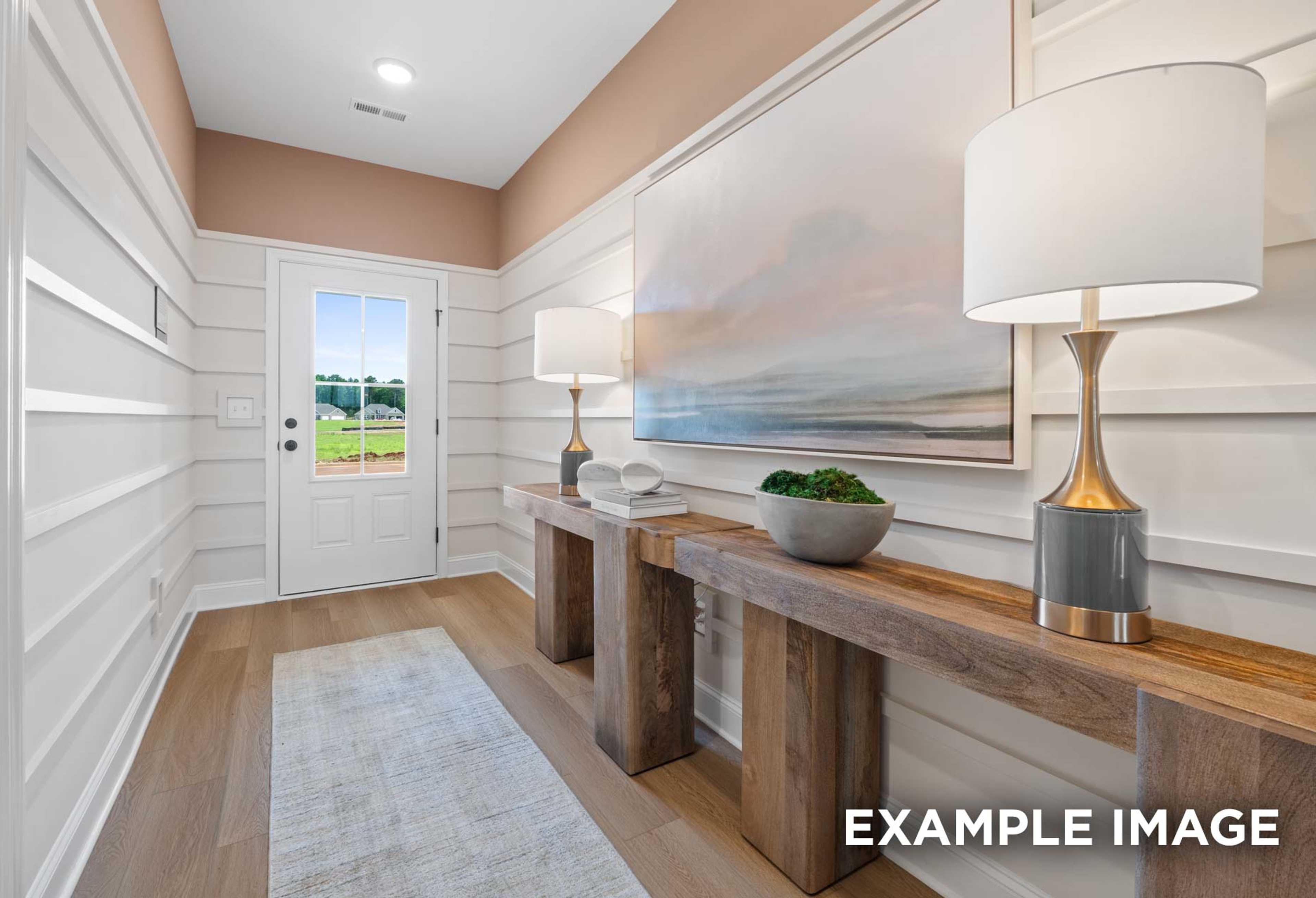 Elegant foyer in The Laurel M home: shiplap walls, abstract seascape art, wooden consoles with lamps, potted plant, baseball field view through door