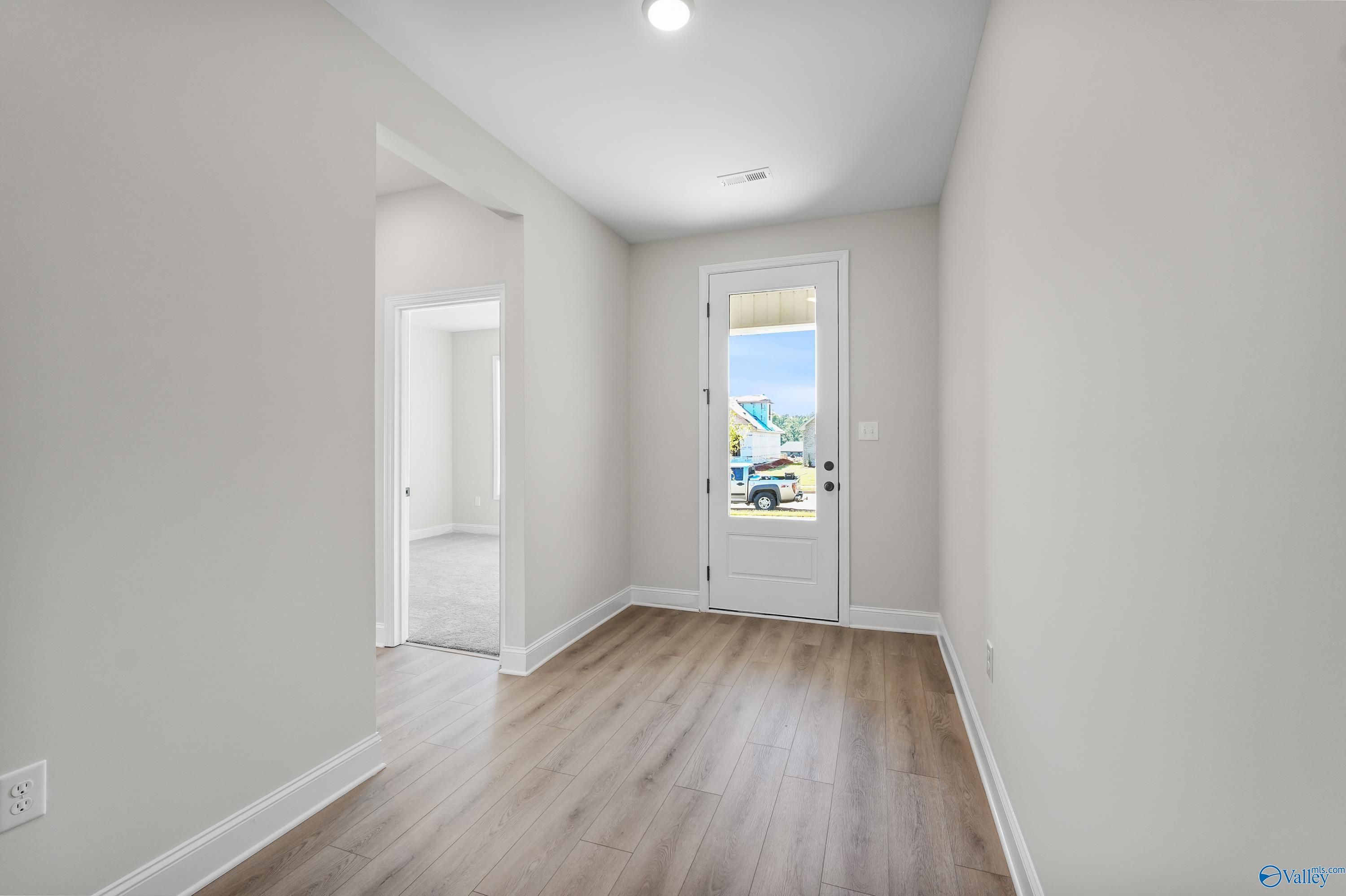 Bright entry hallway with light gray walls, wood flooring, and back door to lush outdoor view in 3-bed Davidson Homes Montgomery C, Decatur AL