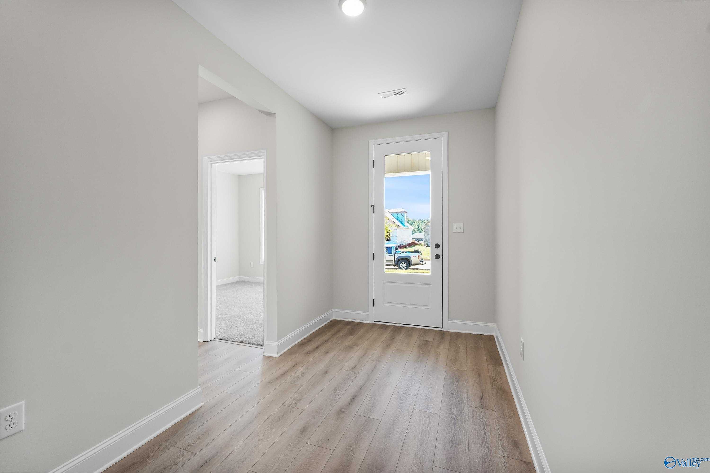 Bright entry hallway with light gray walls, wood flooring, and back door to lush outdoor view in 3-bed Davidson Homes Montgomery C, Decatur AL