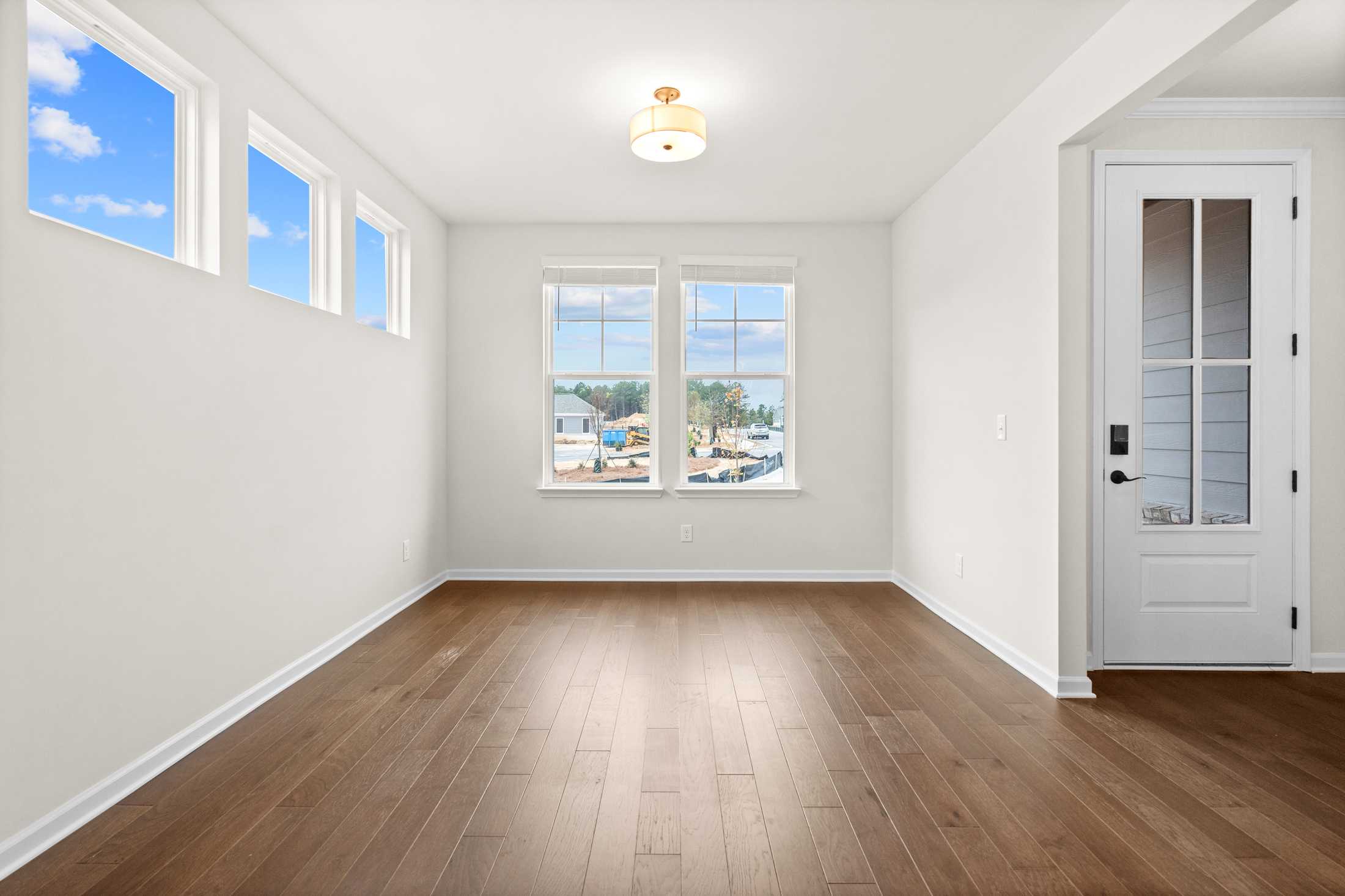 Spacious living room in The Glenwood B home design with large windows, hardwood floors, white walls, and pendant lighting