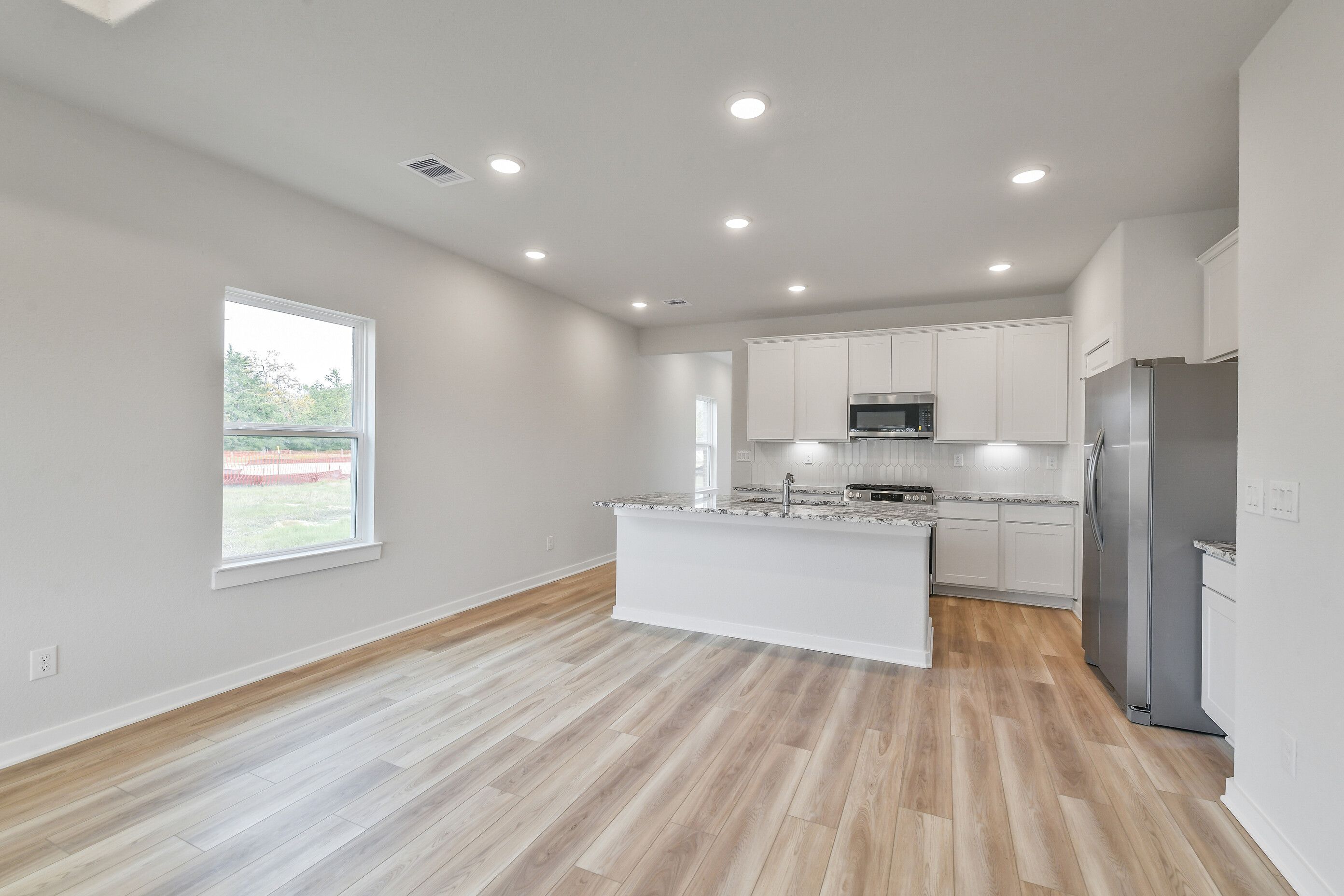 Modern white kitchen with granite island, stainless steel appliances, subway tile backsplash in Davidson Homes The Colorado G, Magnolia TX