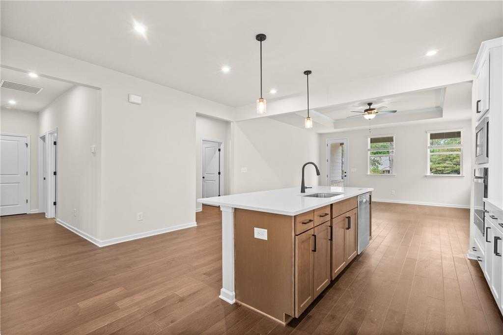 Modern open-concept kitchen with white cabinets, quartz island sink, stainless appliances, and hardwood floors in The Glenwood C, Loganville, GA