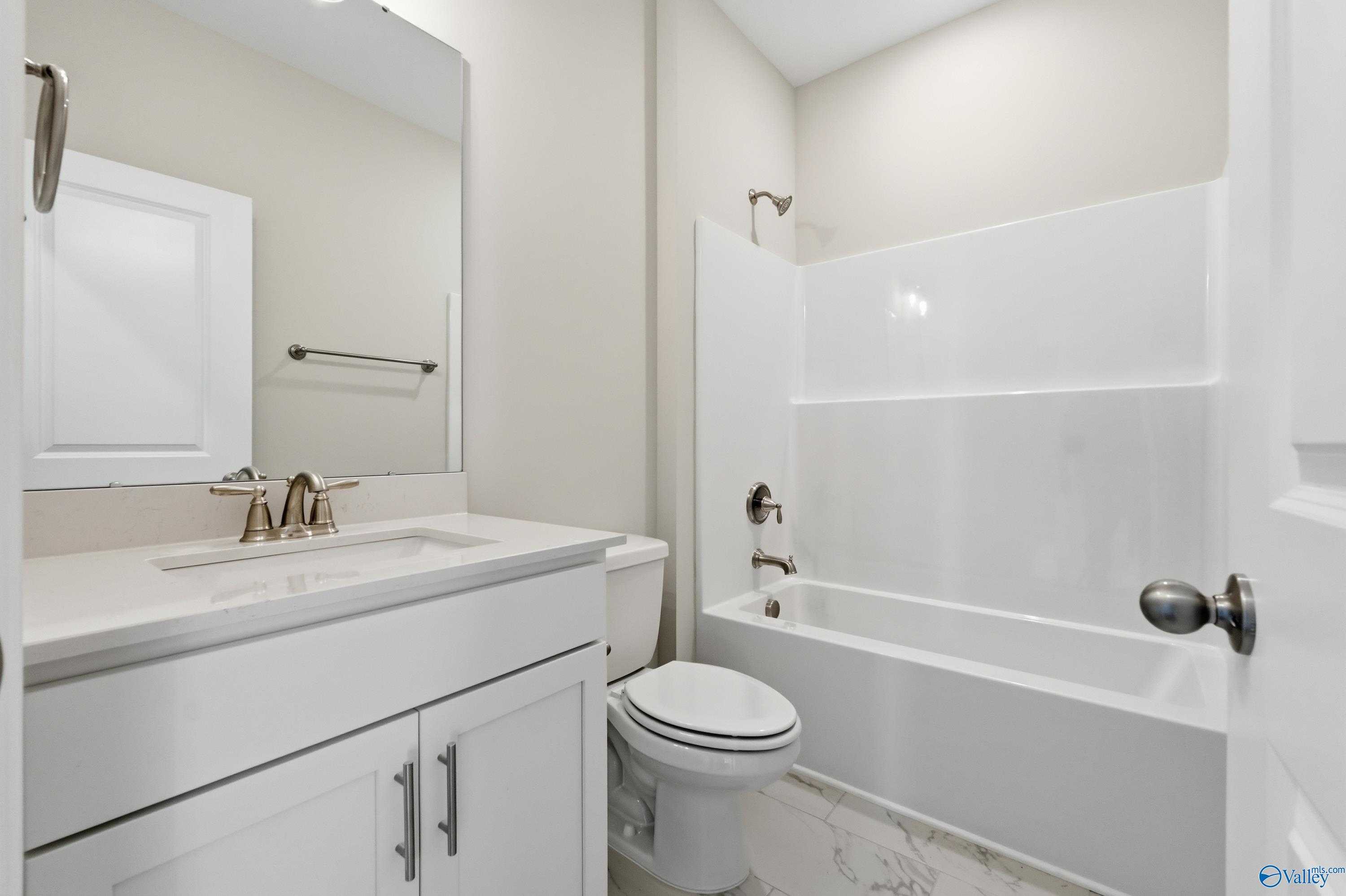 Modern bathroom with white tub-shower combo, vanity, mirror, and toilet in The Montgomery B by Davidson Homes, Toney, Alabama