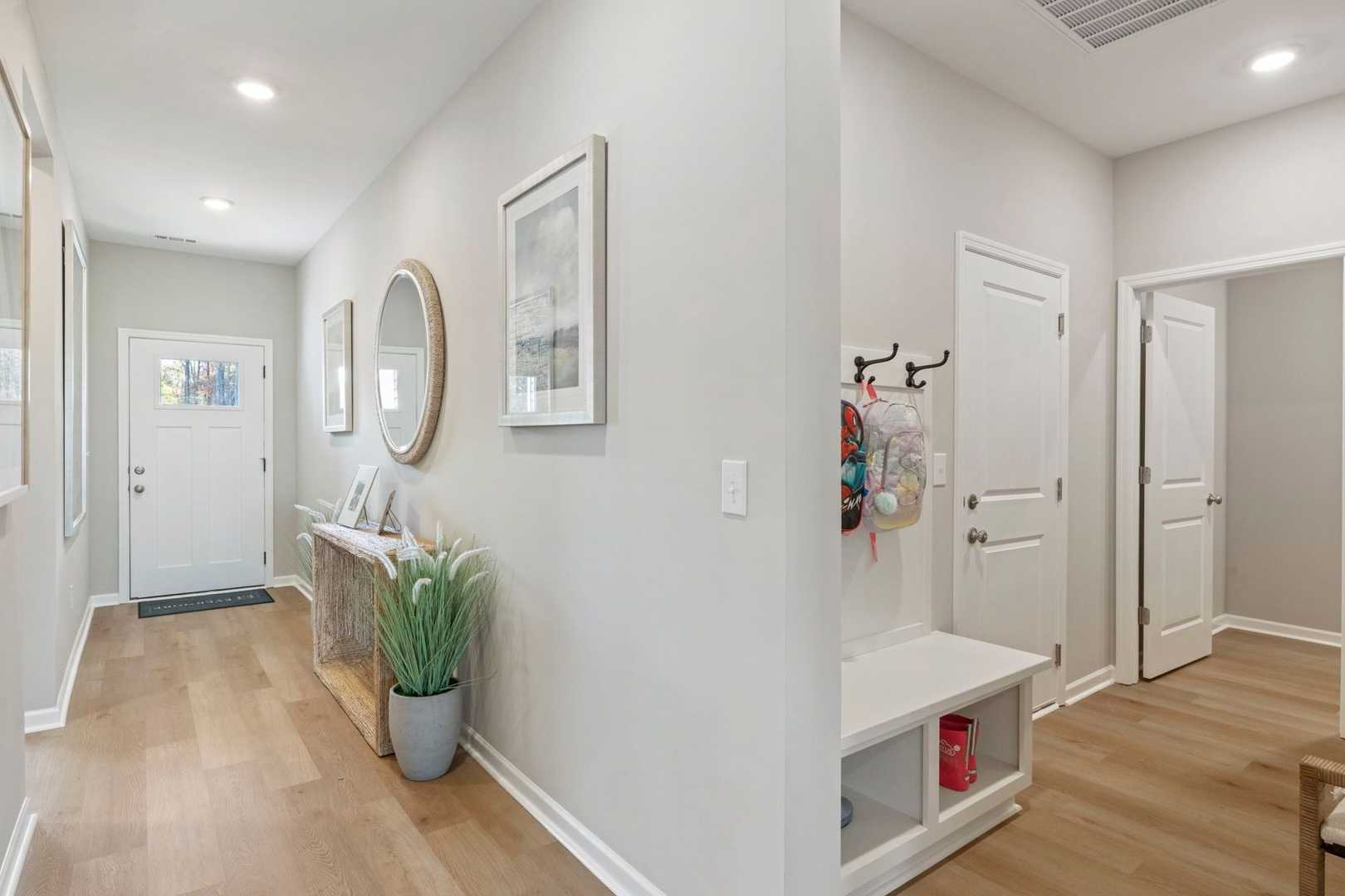 Bright entry hallway in The Phoenix home design featuring console table, potted plants, framed art, coat hooks, and built-in bench