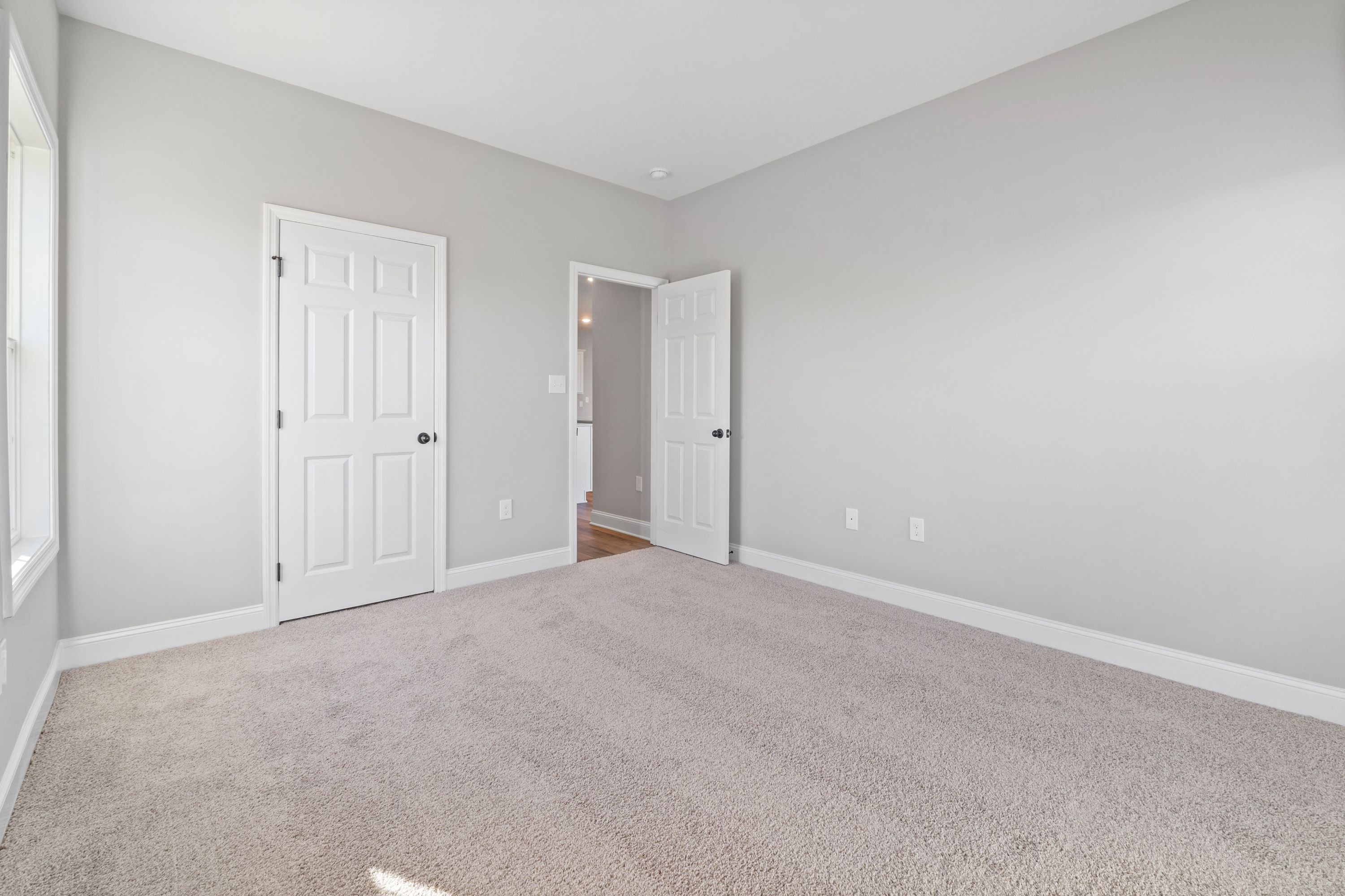 Spacious secondary bedroom in The Valencia with light gray walls, beige carpet, white paneled doors, and ensuite bath access