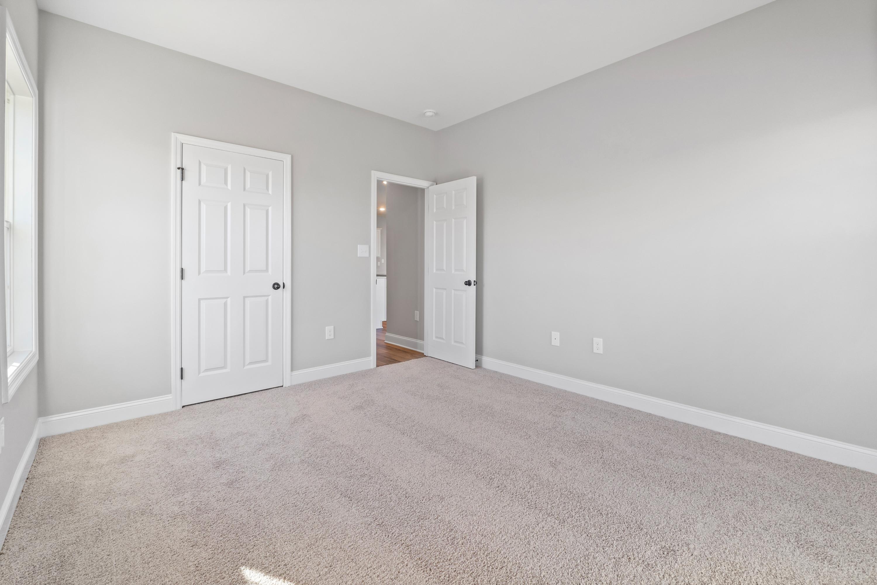 Spacious secondary bedroom in The Valencia with light gray walls, beige carpet, white paneled doors, and ensuite bath access