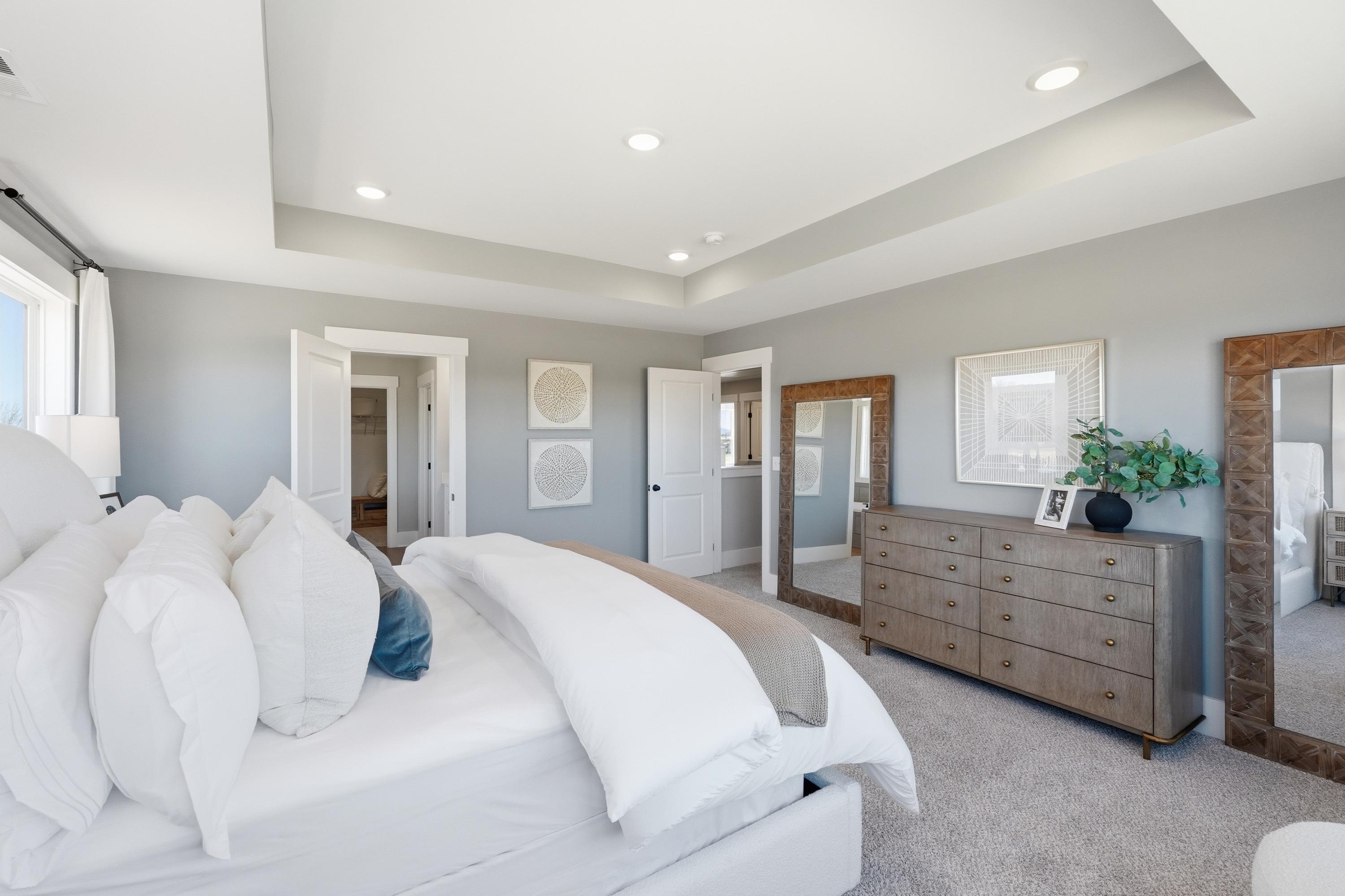 Spacious master bedroom in Berry Cove, New Market AL featuring gray walls, king bed with white duvet, wooden dresser, and mirrors