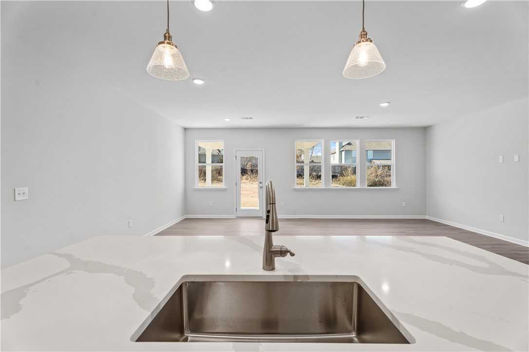 Modern white quartz kitchen island with stainless sink and pendant lights in open-concept The Luna B home, Opelika, Alabama