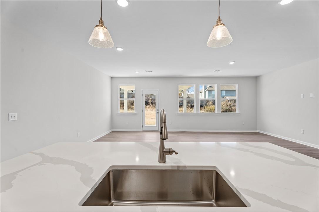 Modern white quartz kitchen island with stainless sink and pendant lights in open-concept The Luna B home, Opelika, Alabama
