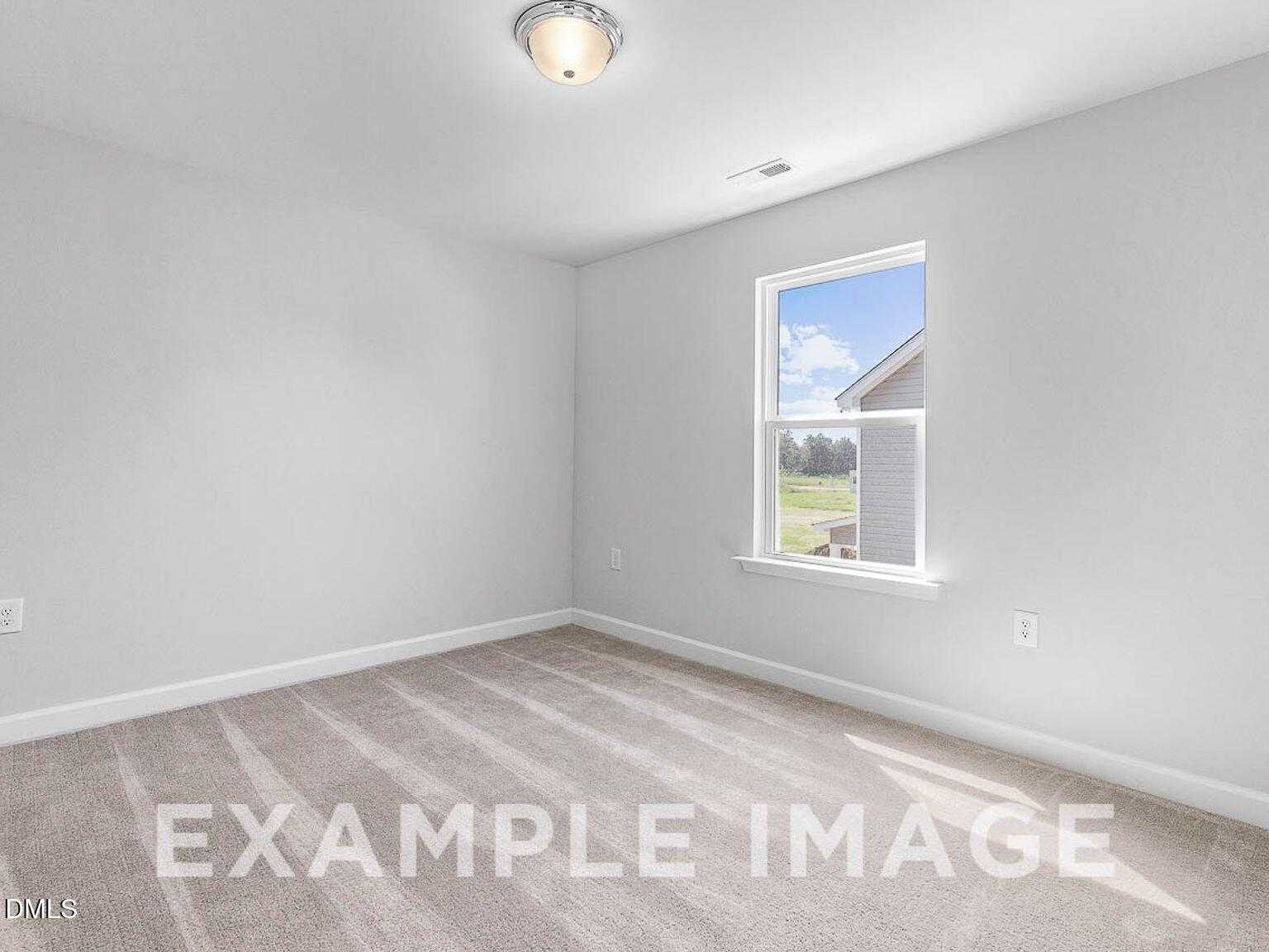 Bright empty bedroom with gray walls, beige carpet, and window view of blue sky in The Chestnut B home, Lillington, NC