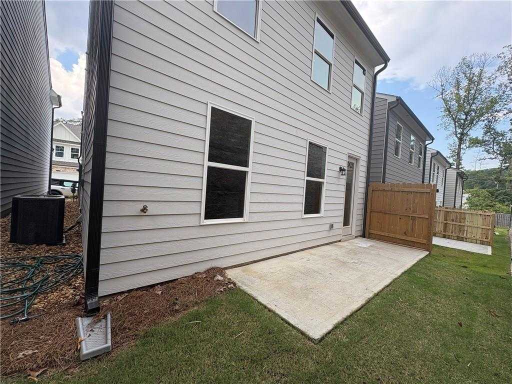 Side view of The Marion B two-story home with gray siding, large windows, concrete patio, and wooden fence in The Village at Shallowford, Kennesaw