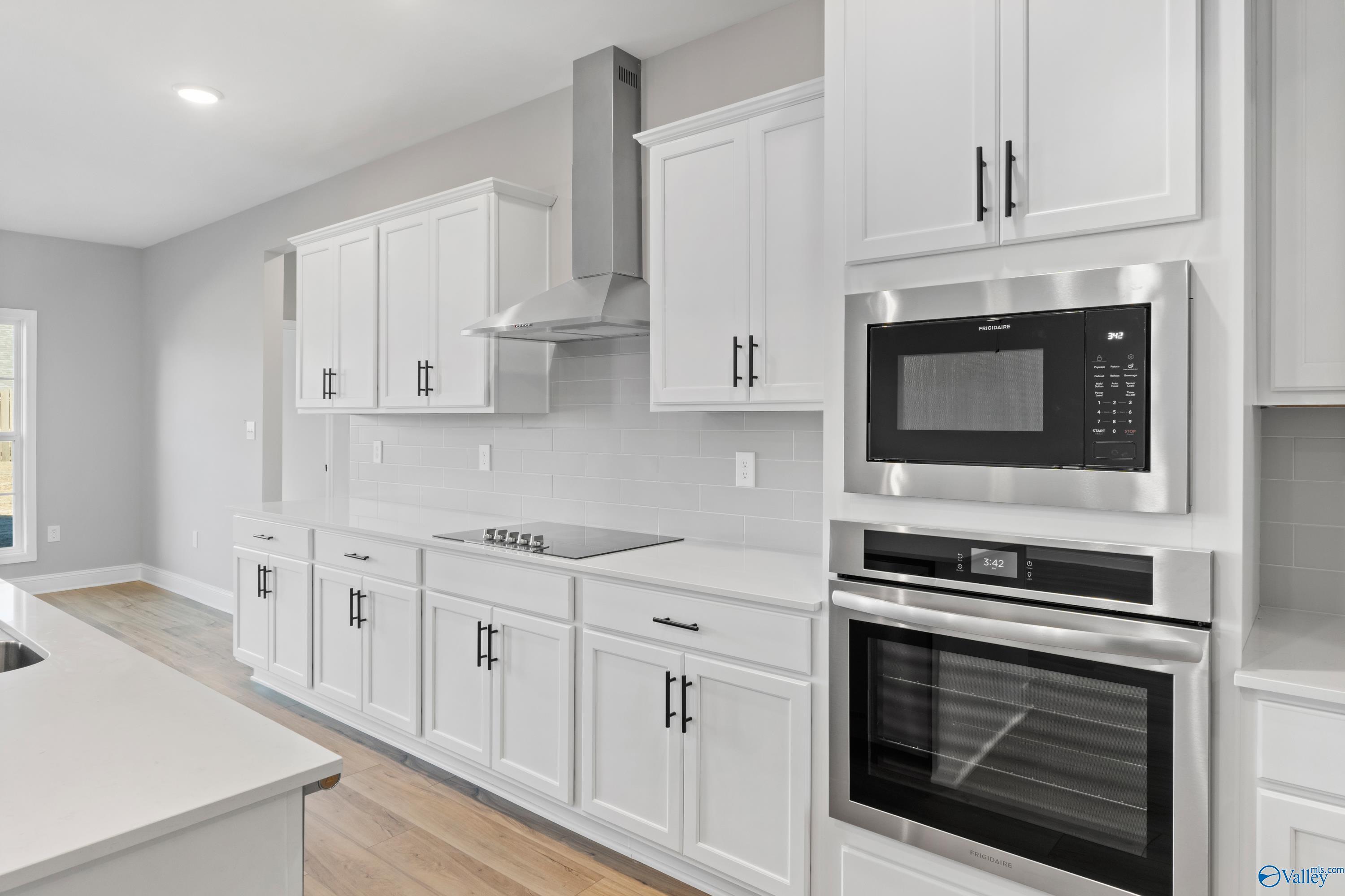 Modern white kitchen with stainless steel appliances, quartz island, and cabinets in Davidson Homes The Valencia, Meridianville, AL