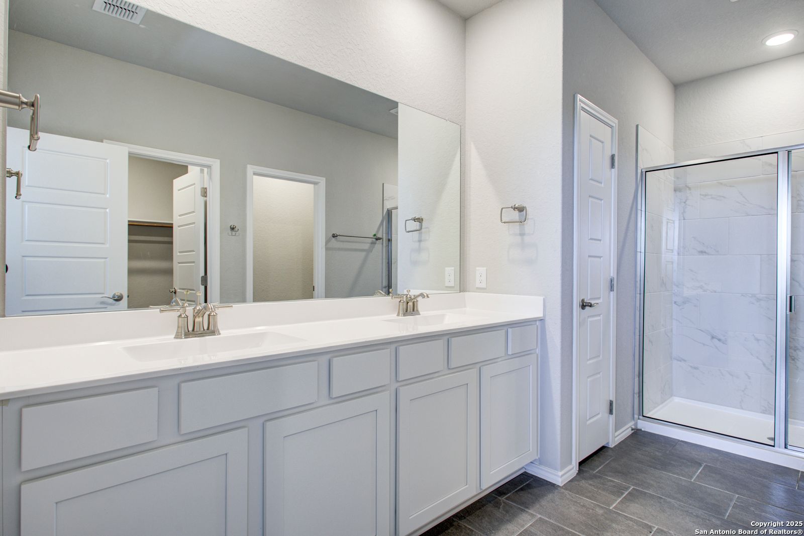 Luxurious master bathroom with double quartz vanity, white shaker cabinets, and frameless glass walk-in shower in Davidson Homes The Douglas G, San Antonio