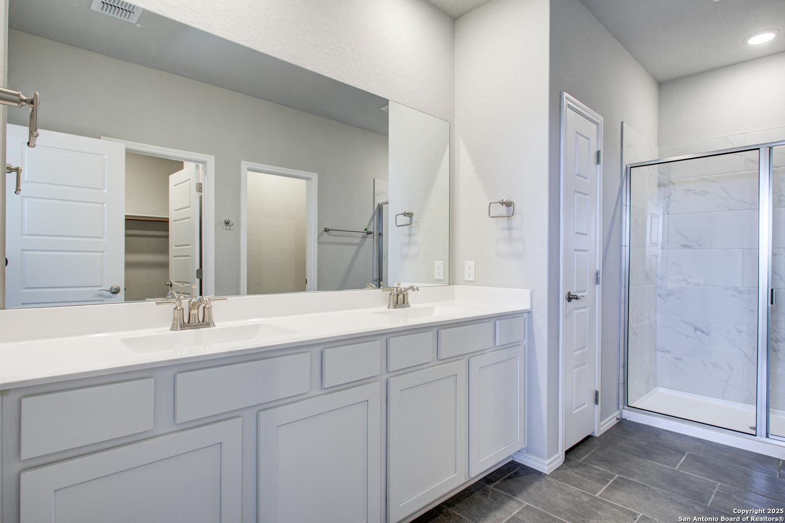 Luxurious master bathroom with double quartz vanity, white shaker cabinets, and frameless glass walk-in shower in Davidson Homes The Douglas G, San Antonio