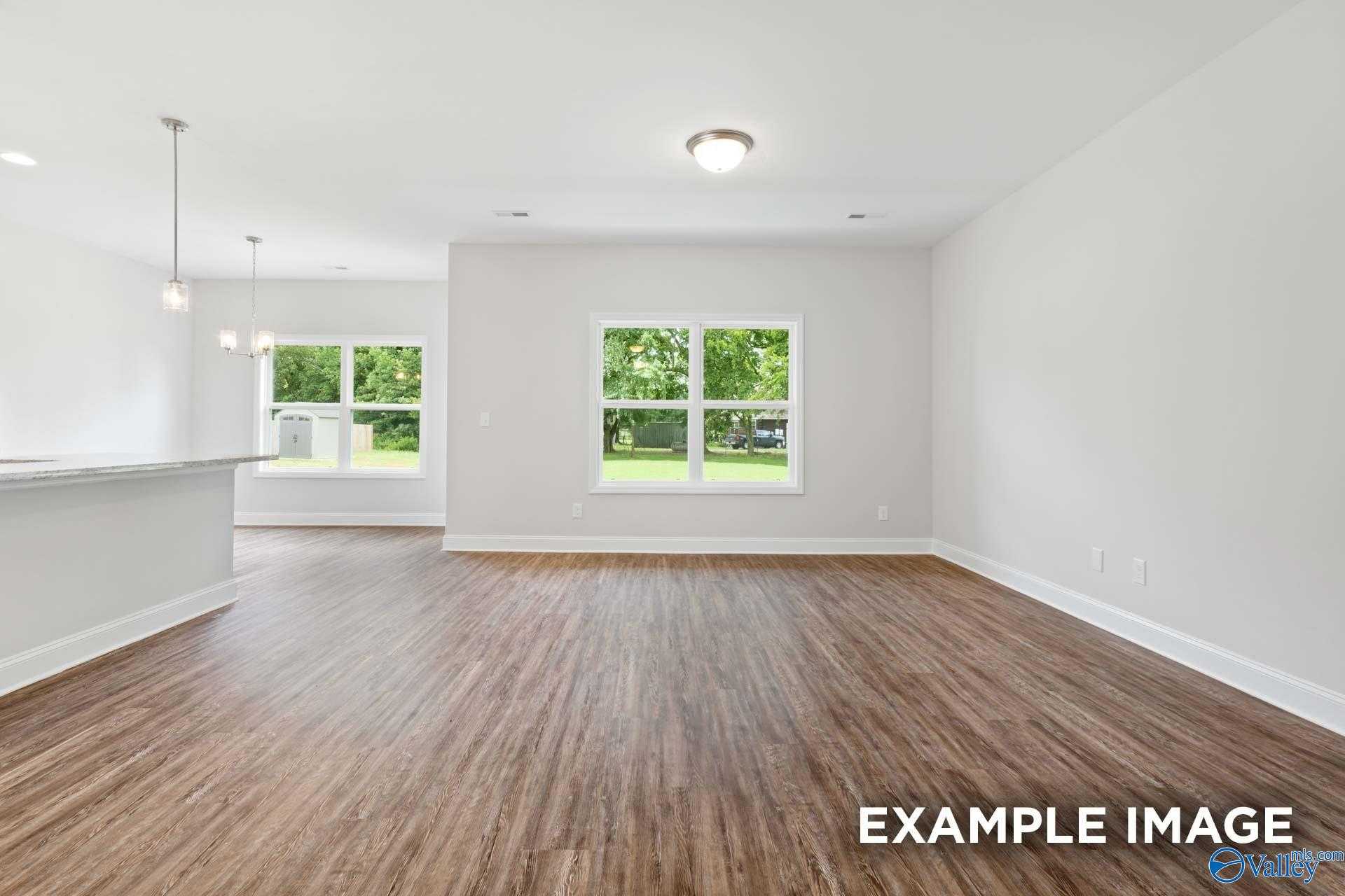 Spacious open living room with hardwood floors, large windows overlooking green yard, and kitchen bar in The Asheville C home, Meridianville, Alabama