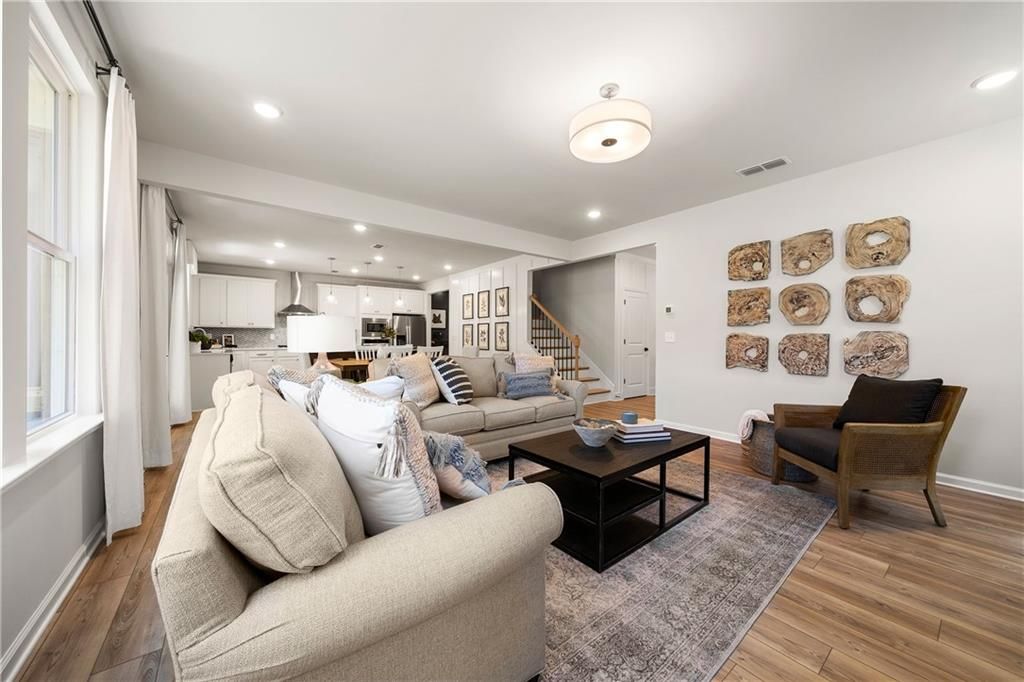 Cozy living room with beige sectional sofa, coffee table, armchair, staircase, and open kitchen in Davidson Homes The Willow B 5-bedroom home, Riverwood, Dallas, Georgia