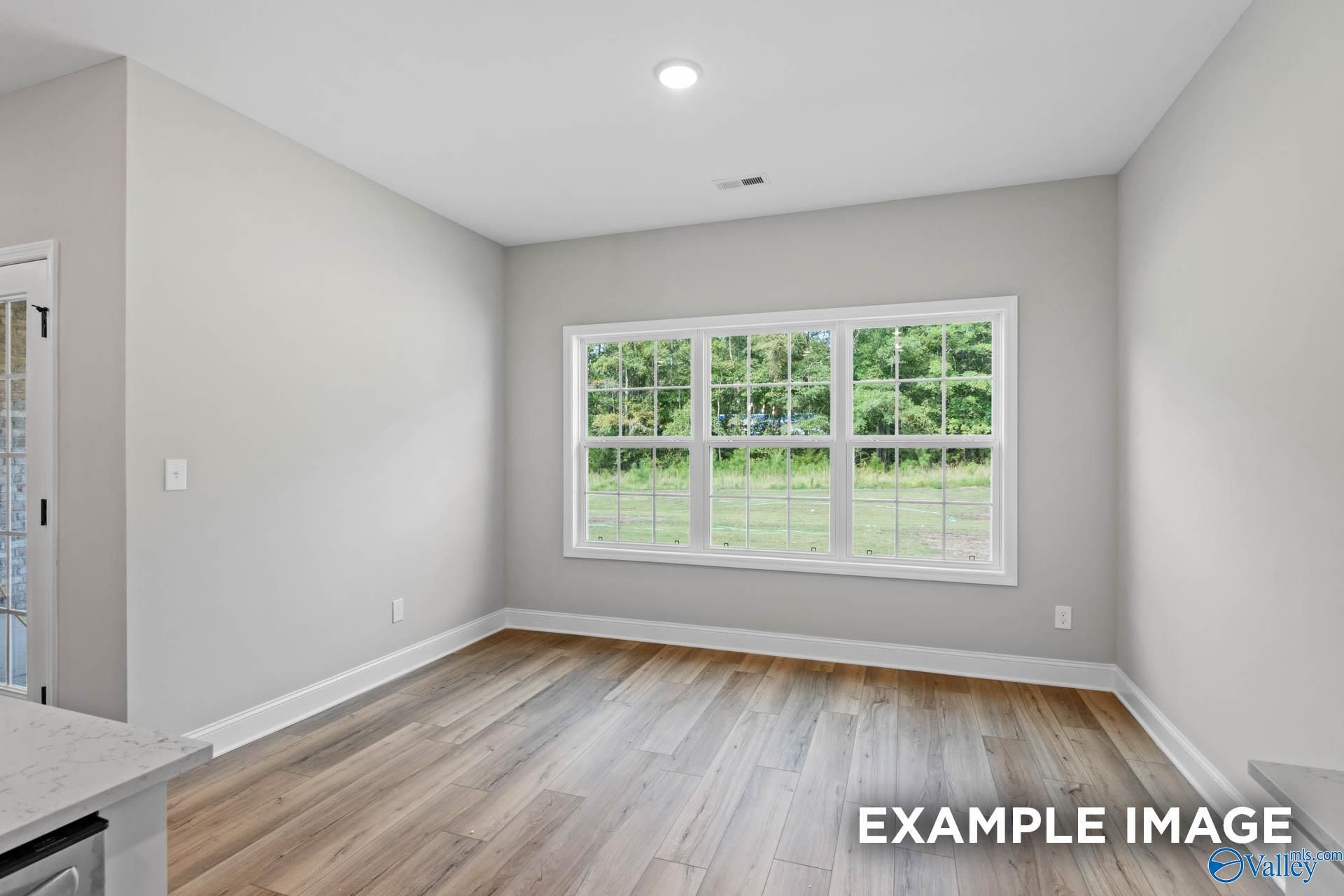 Bright secondary bedroom with hardwood floors and large window overlooking lush green lawn in Davidson Homes Montgomery B, Toney, Alabama