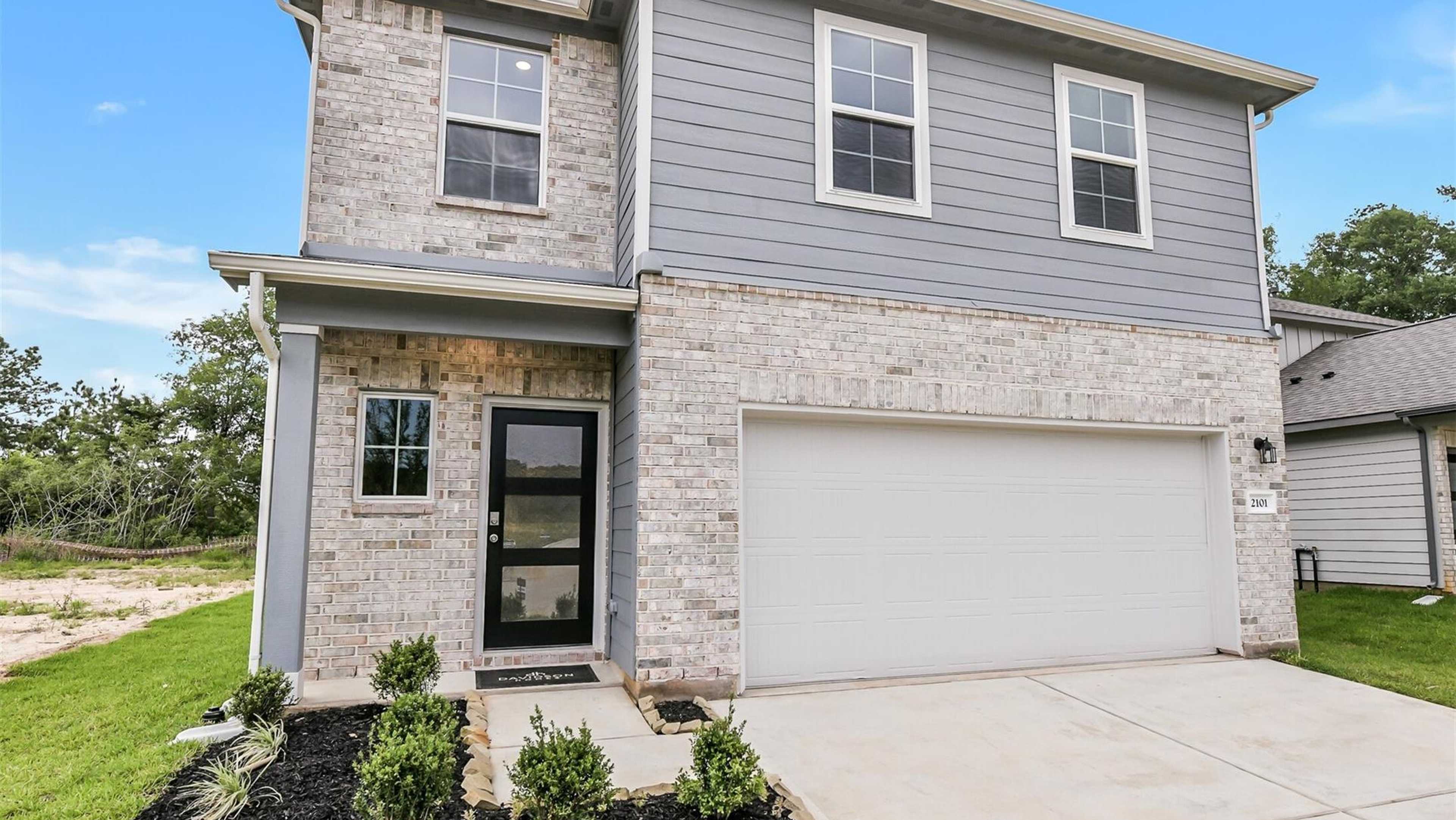 Modern two-story brick home with gray siding, garage, and landscaped front yard at Davidson Homes open house on Caney Creek Lane