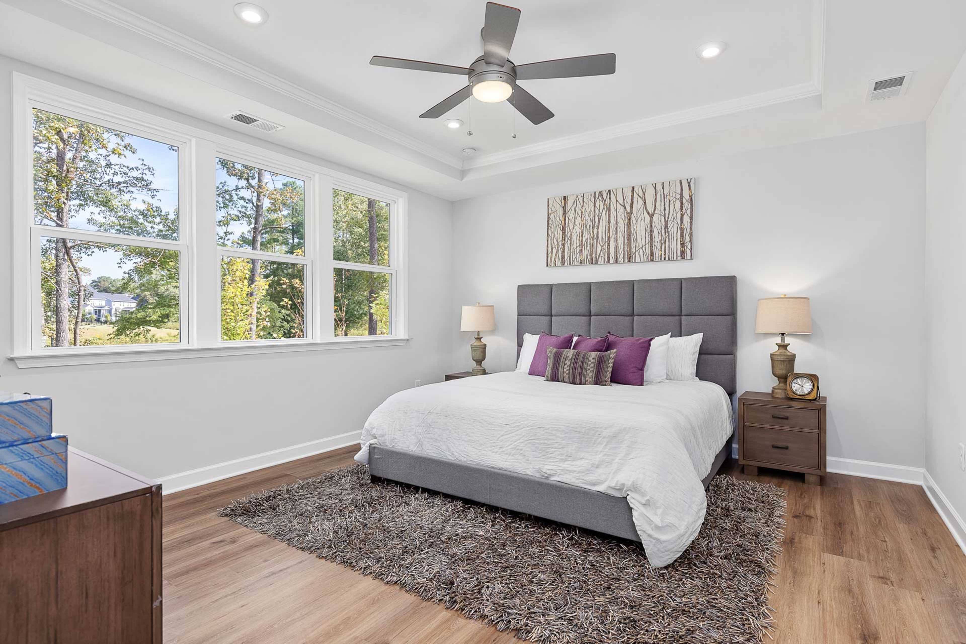 Elegant master bedroom at Glenmere in Knightdale NC with king bed, hardwood floors, ceiling fan, and large windows