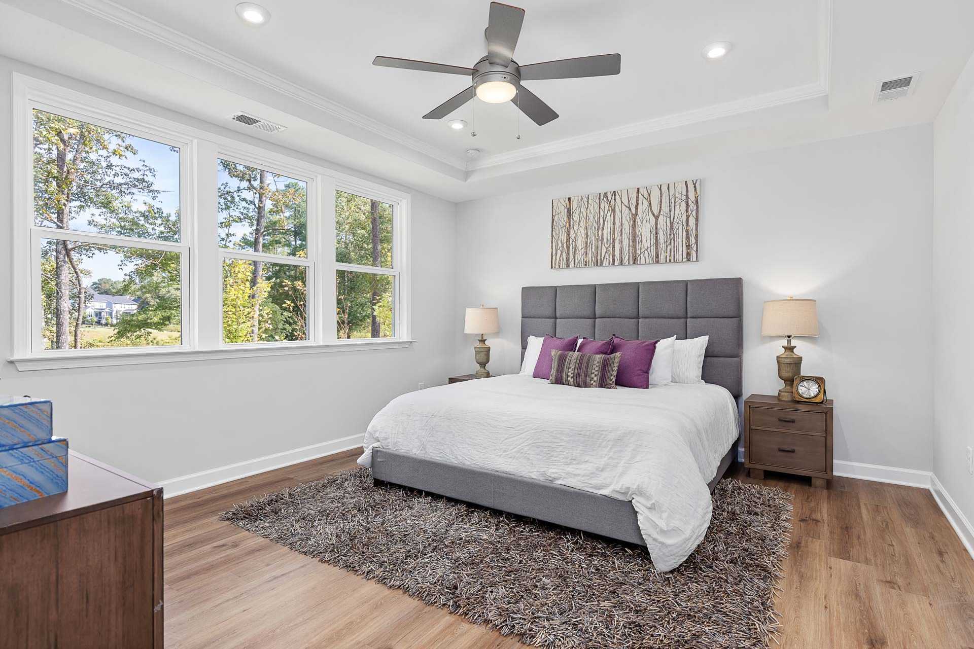 Elegant master bedroom at Glenmere in Knightdale NC with king bed, hardwood floors, ceiling fan, and large windows