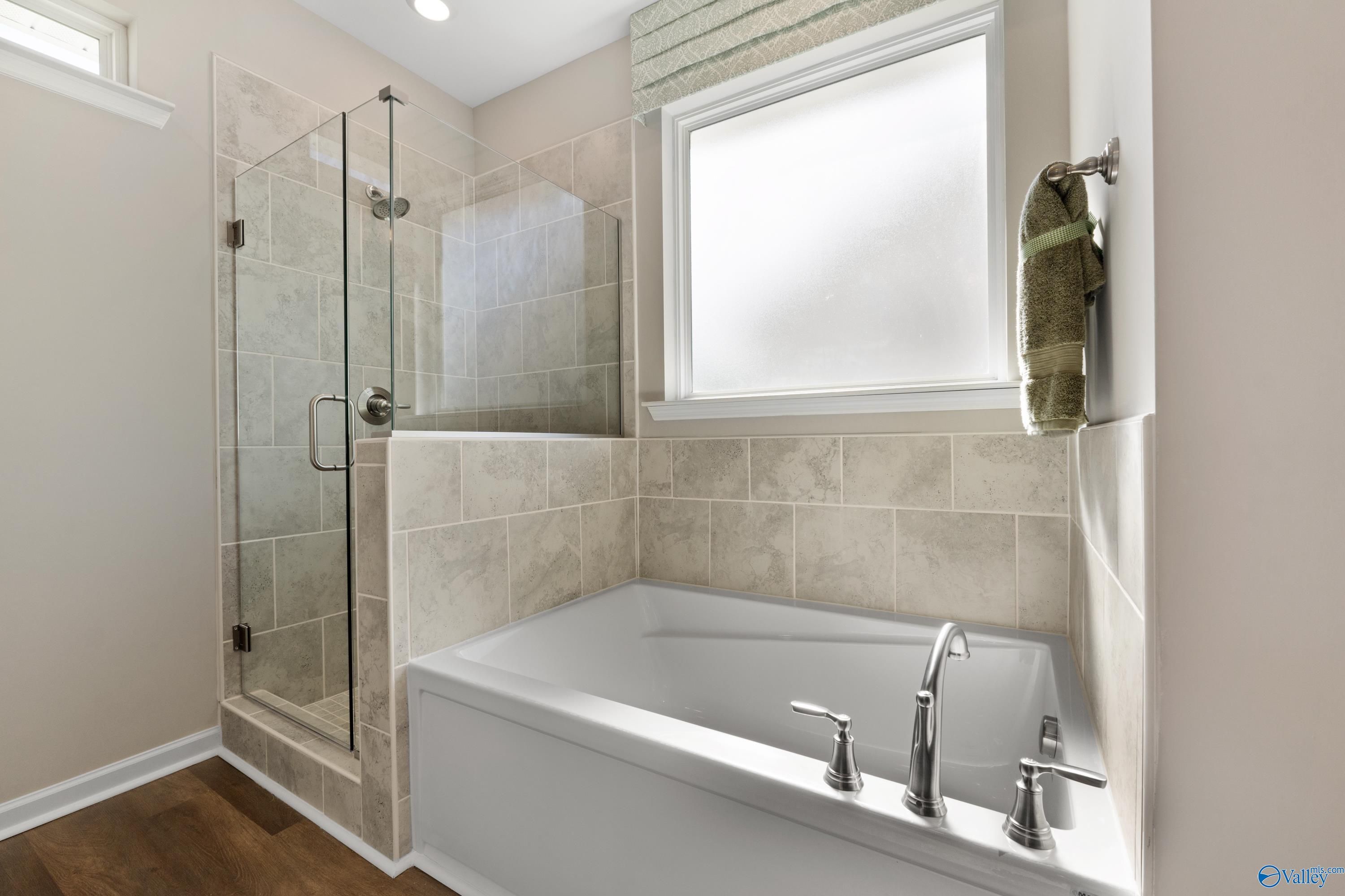 Elegant master bathroom featuring glass shower, soaking tub, tiled walls, and frosted window in Davidson Homes The Stella, Madison, Alabama