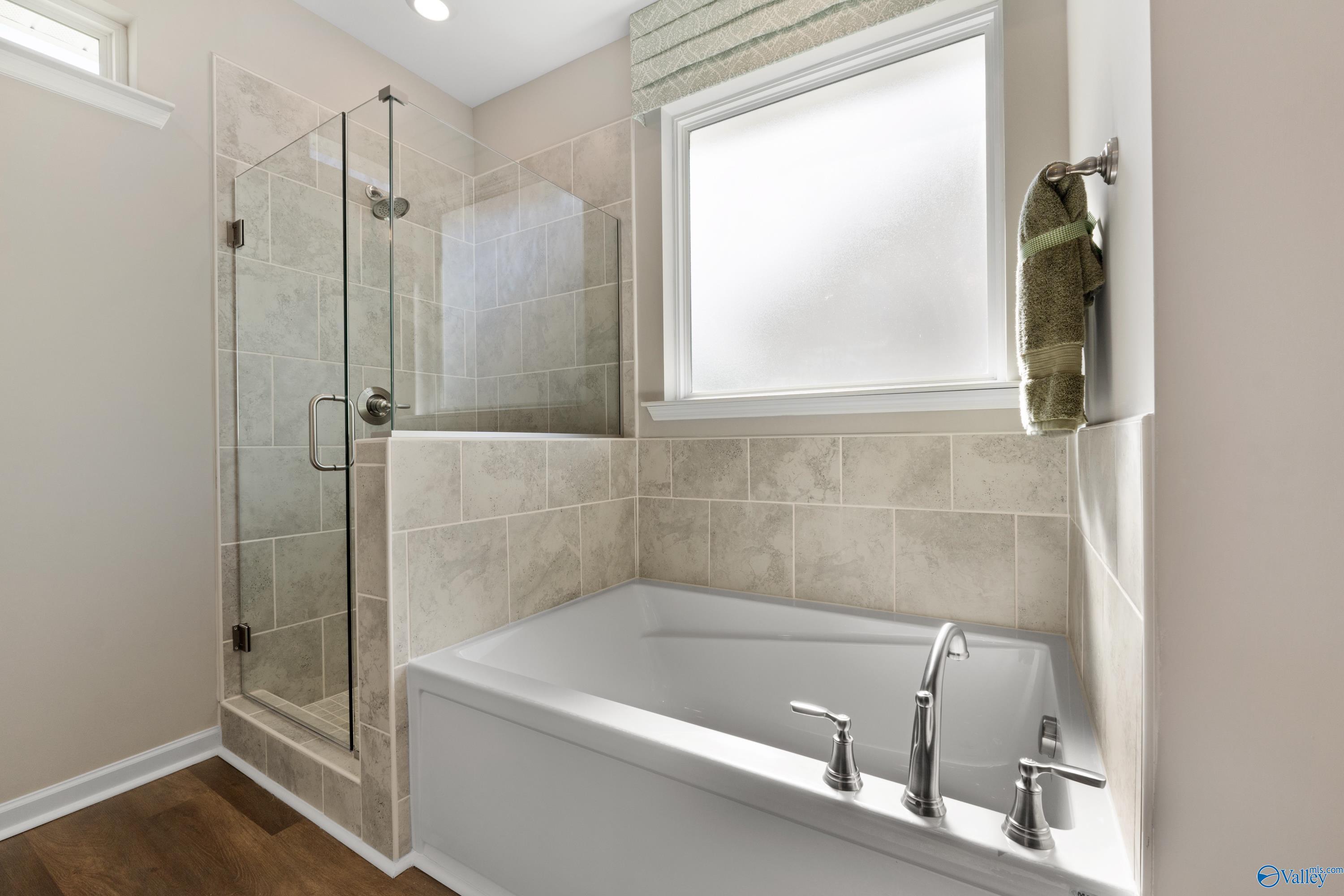 Elegant master bathroom featuring glass shower, soaking tub, tiled walls, and frosted window in Davidson Homes The Stella, Madison, Alabama