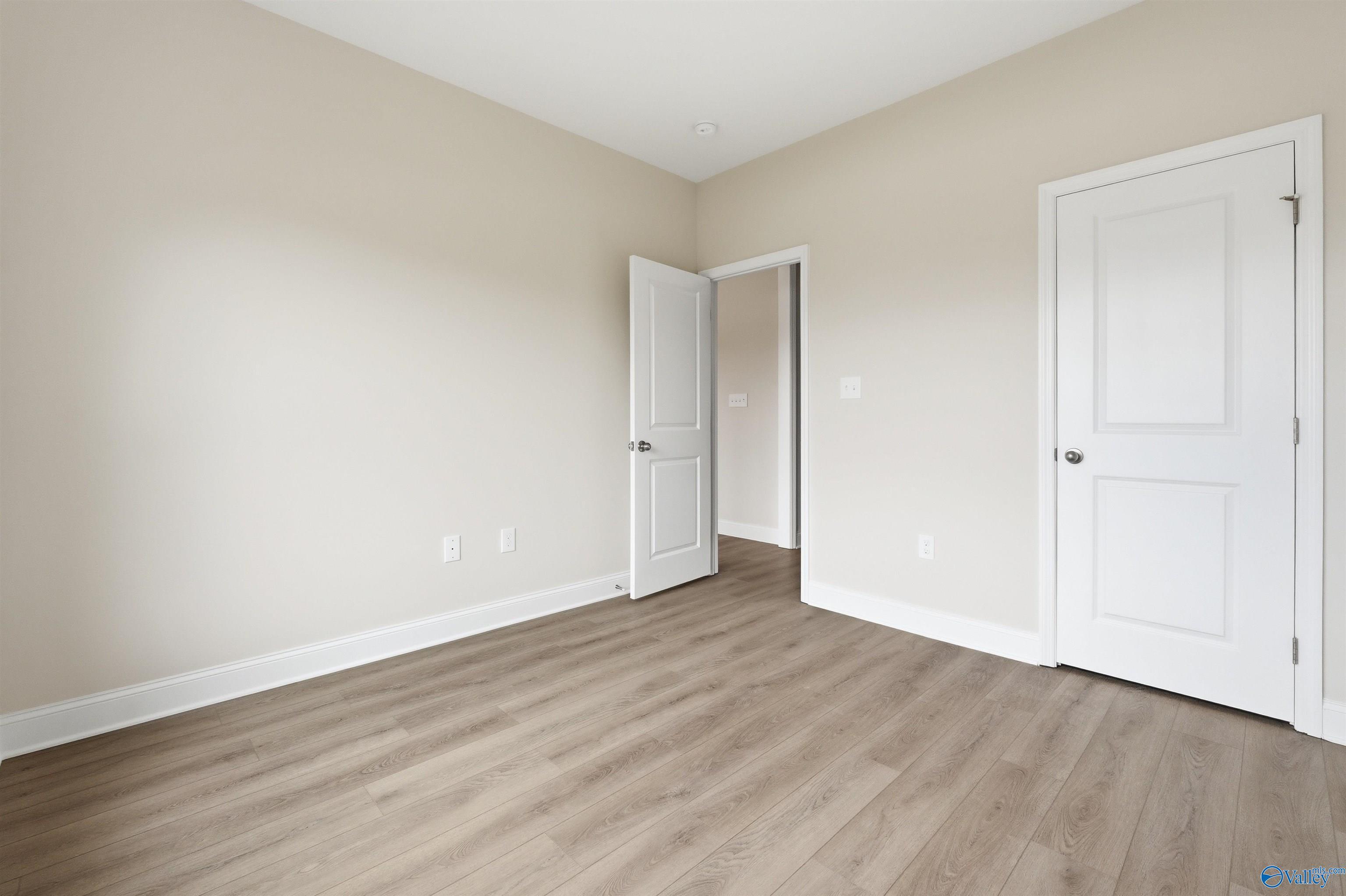 Spacious bedroom with light wood-style flooring in The Shelby D floor plan at Evergreen Mill, Madison, Alabama.