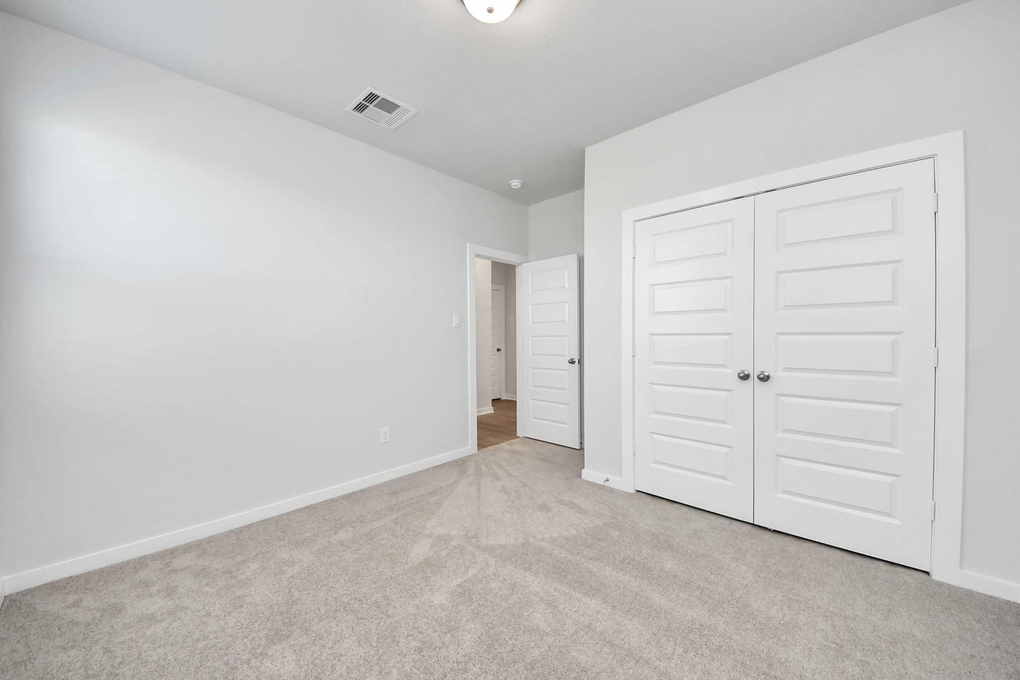 Bright bedroom with plush carpet and double-door closet in Davidson Homes' The Costa A floor plan, Emberly, Beasley, Texas