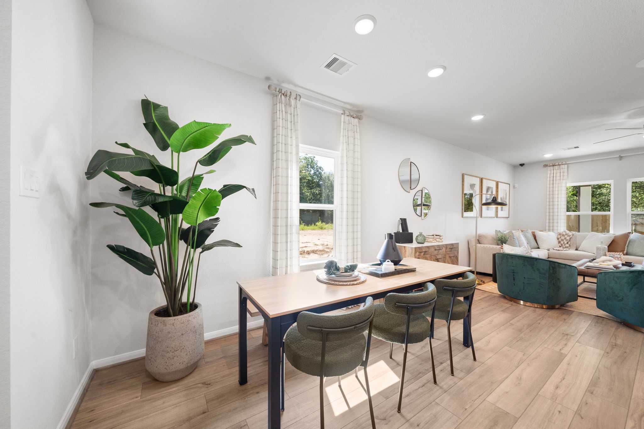 Spacious open-concept dining and living area at Caney Creek Place in Conroe Texas by Davidson Homes with hardwood floors potted plant and modern seating