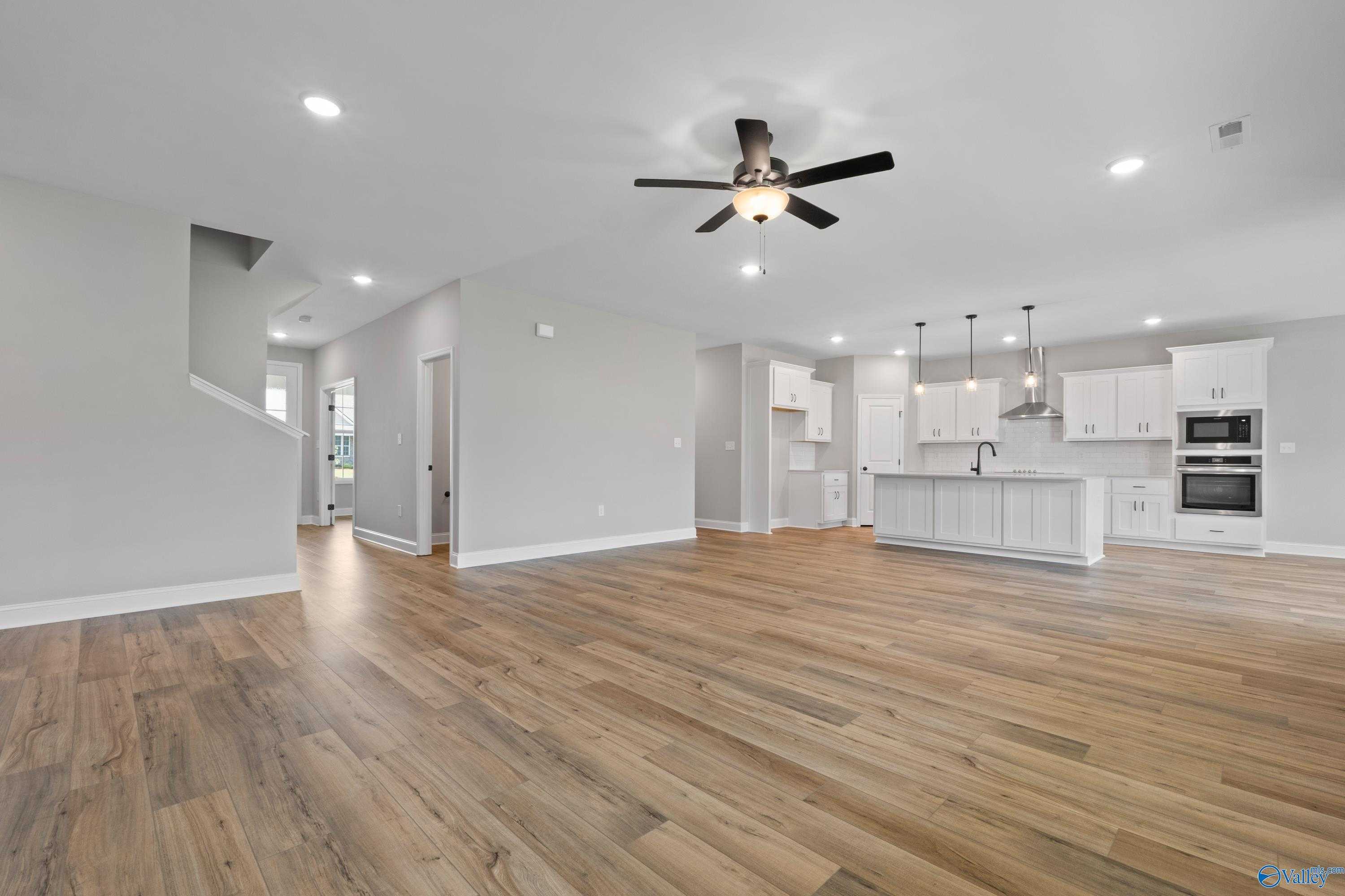 Open-concept kitchen-living space with hardwood floors, white shaker cabinets, and ceiling fan in Davidson Homes The Rockford, Toney, AL